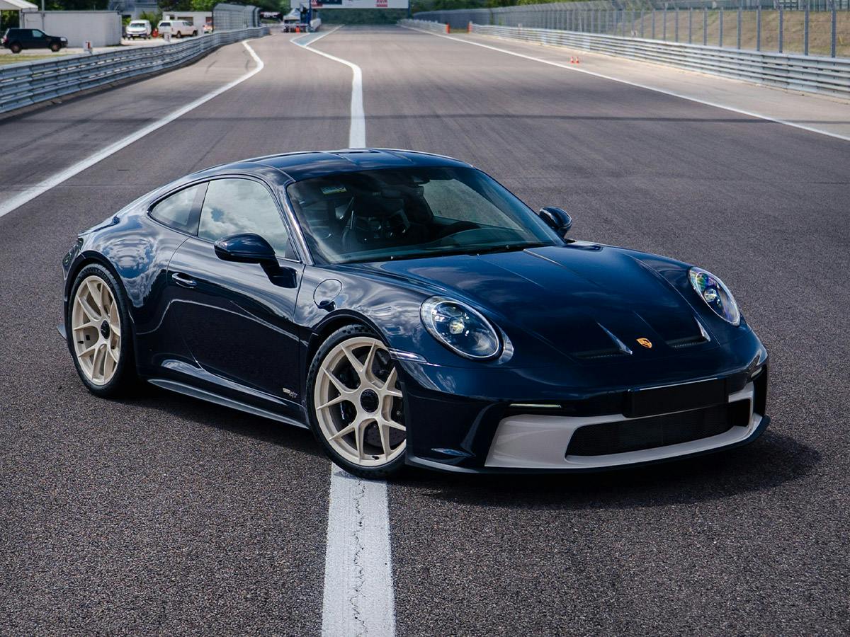 Front three-quarter view of a Porsche 911 S/T in Paint to Sample colour Darkseablue with Creamwhite accents and a customized Graphiteblue interior, positioned on the starting line of Circuit Dijon-Prenois racetrack.