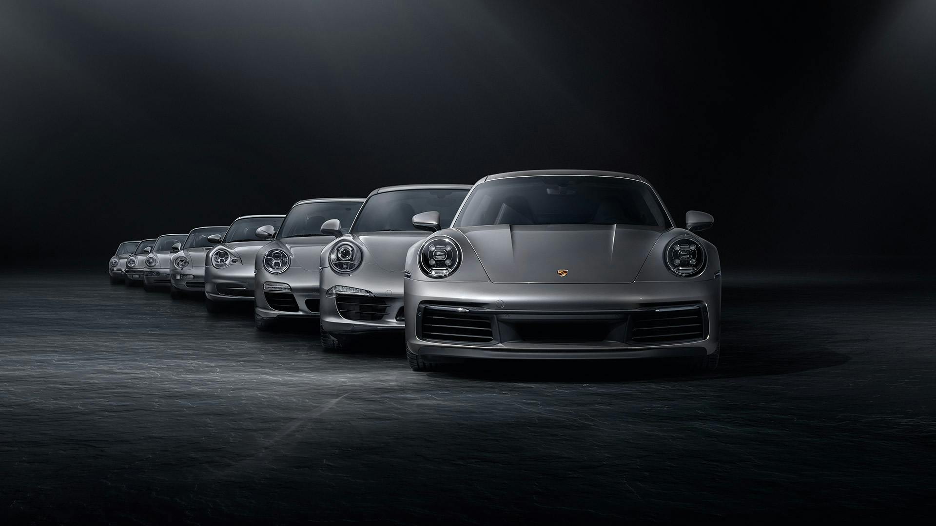 Dans un studio noir, plusieurs modèles de Porsche 911 de génération argentée sont alignés les uns derrière les autres.