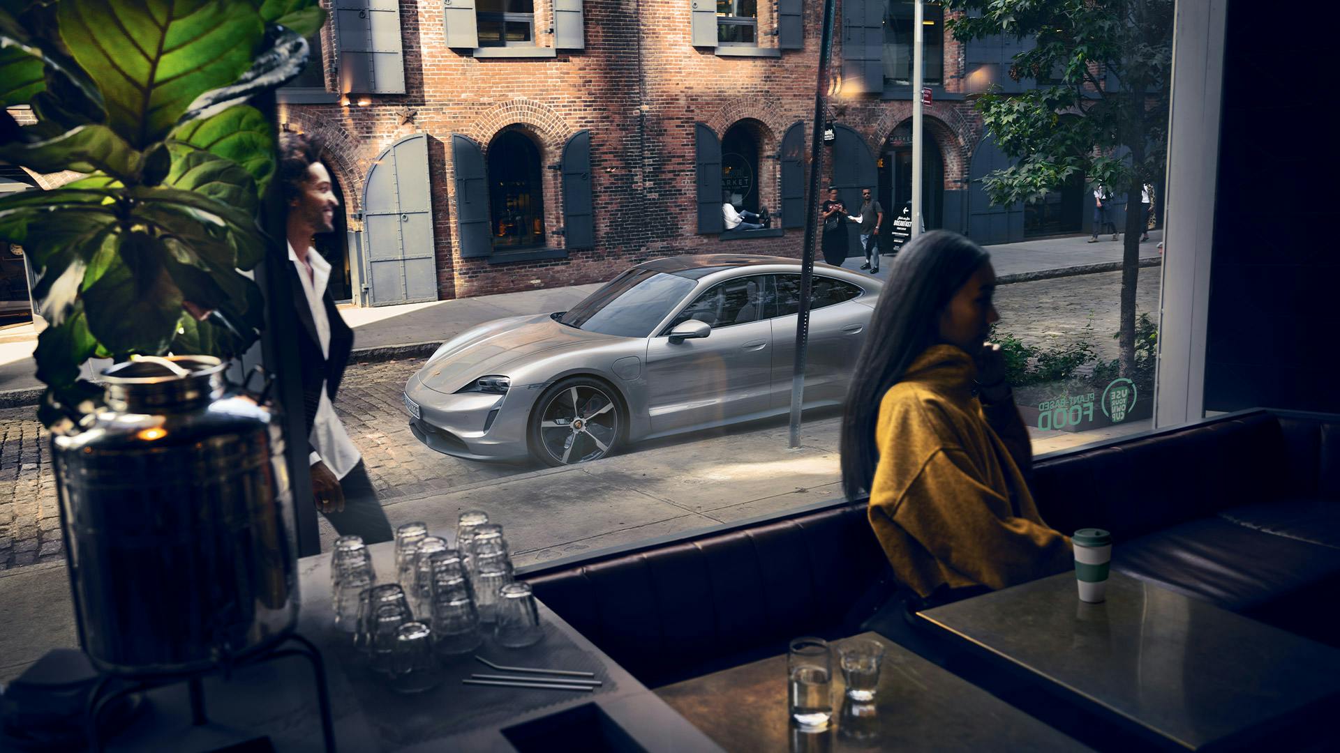 Femme prenant un café avec sa Porsche Taycan argentée garée à proximité.