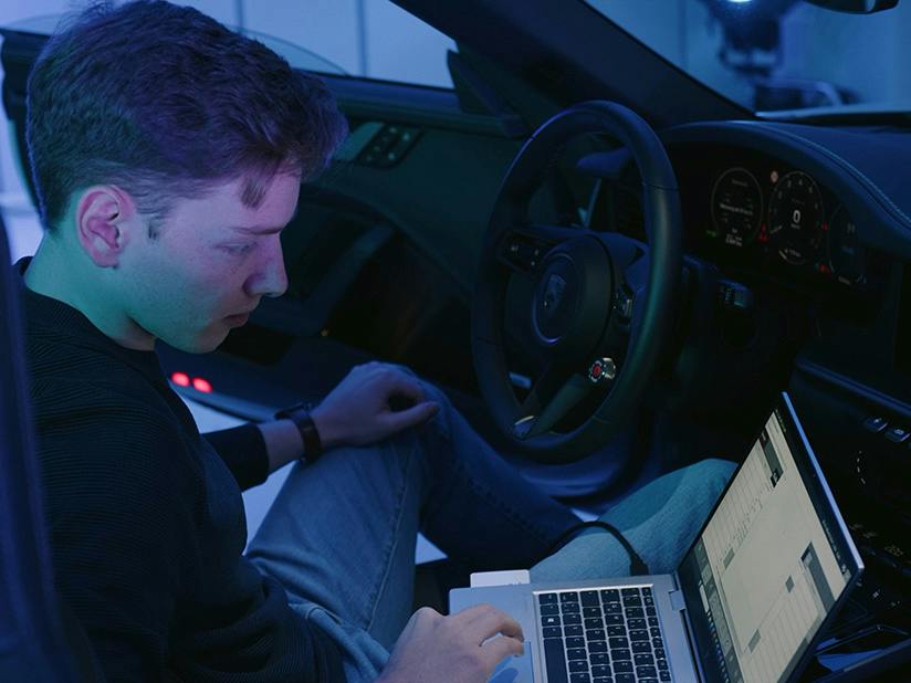 Der Porsche Mitarbeiter Christian sitzt in einem Porsche und prüft Analysedaten am Laptop.