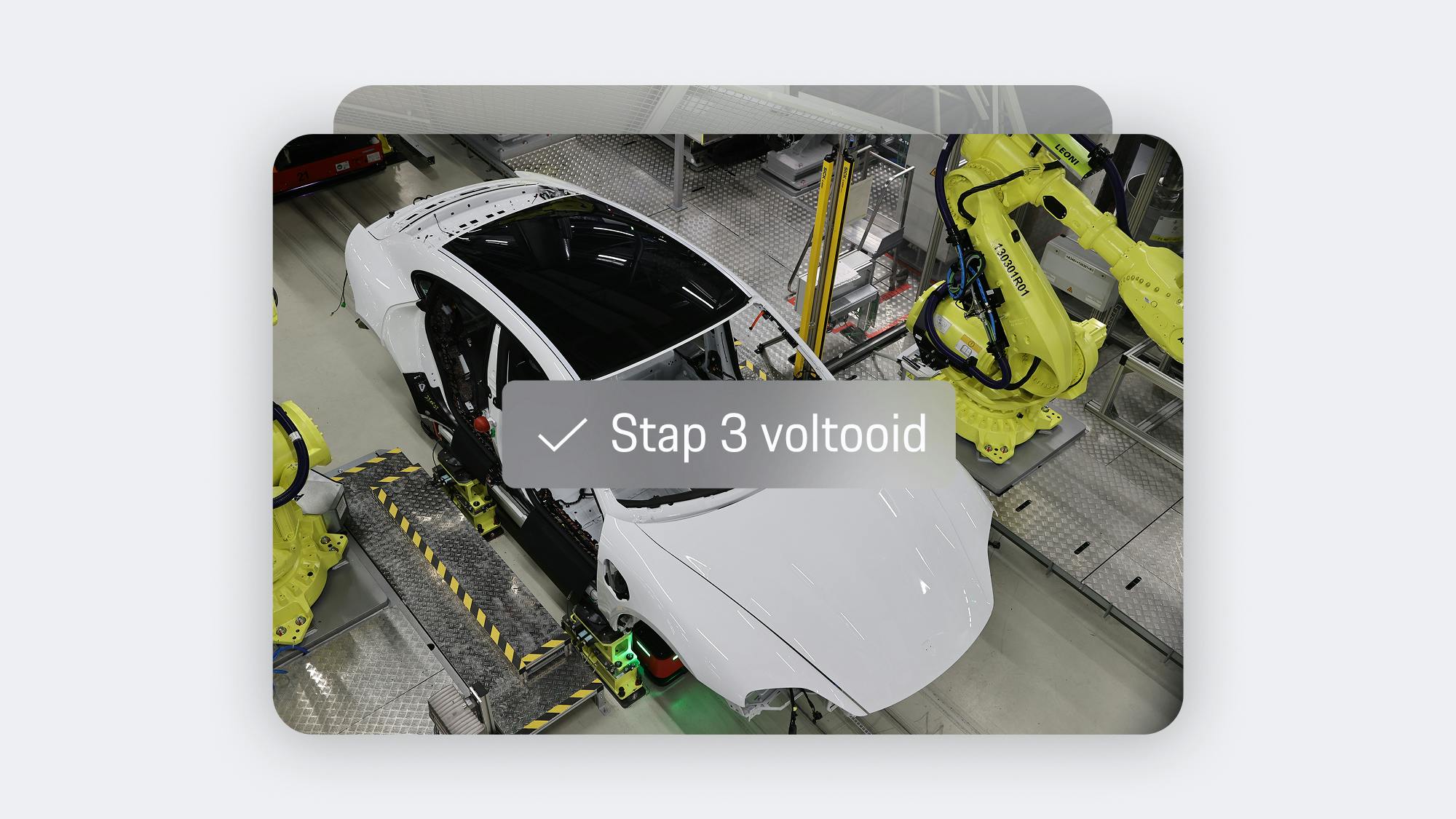 App-weergave van een productiestap: witte Porsche carrosserie op de assemblagelijn met gele robotarmen en de tekst 'Stap 3 voltooid'.