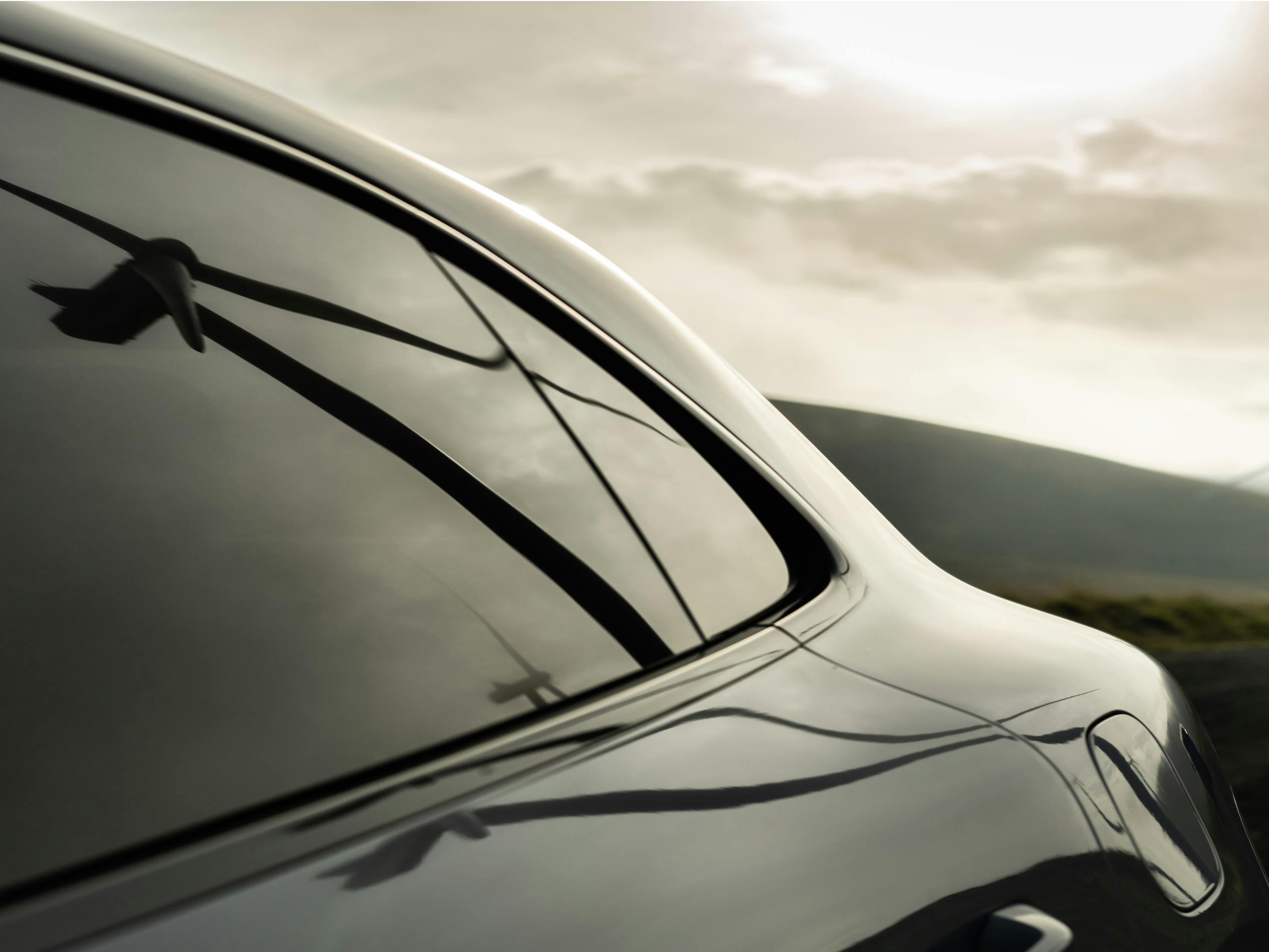 Cloudy but sunny sky reflected in the rear window of a Porsche.