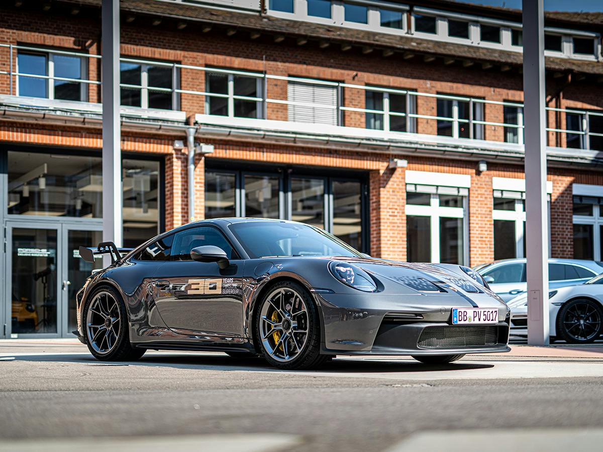 Porsche 911 GT3 “30 Years Supercup” edition in silver in front of brick facade with yellow brake calipers.