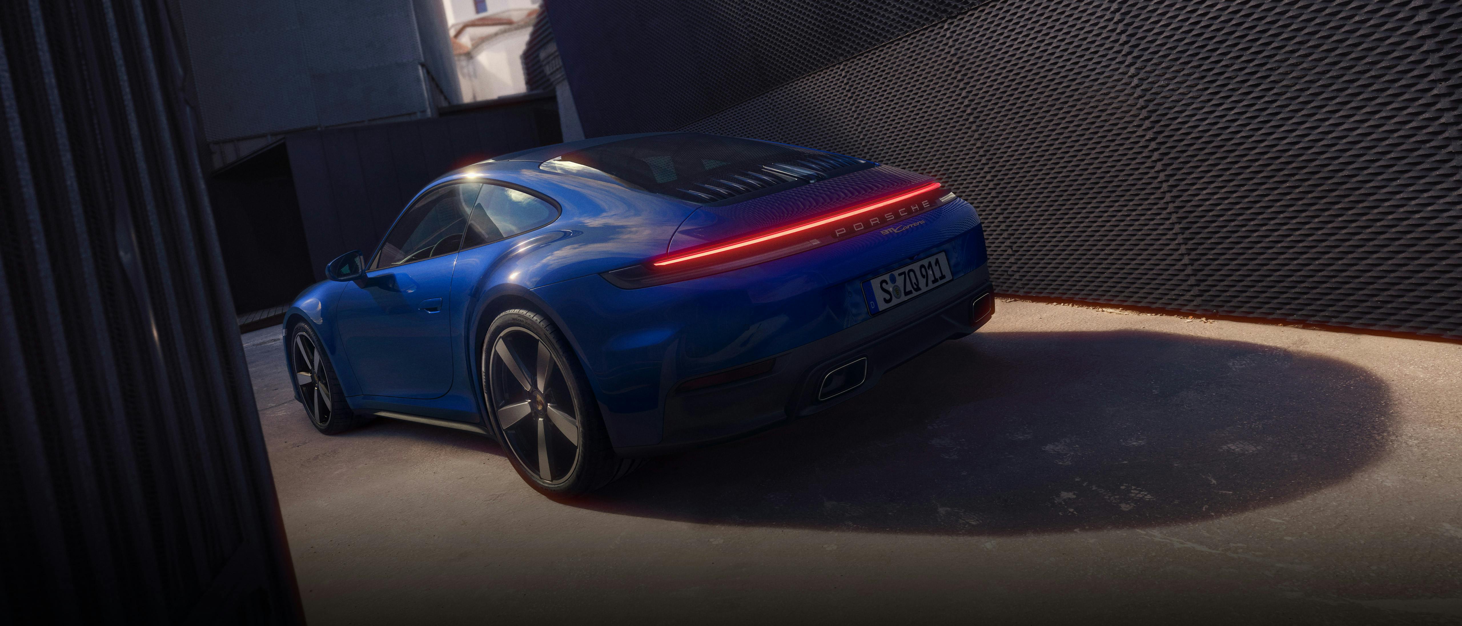 The 911 Carrera parked near a black fence. The Porsche light strip at the rear of the car is lit red.​