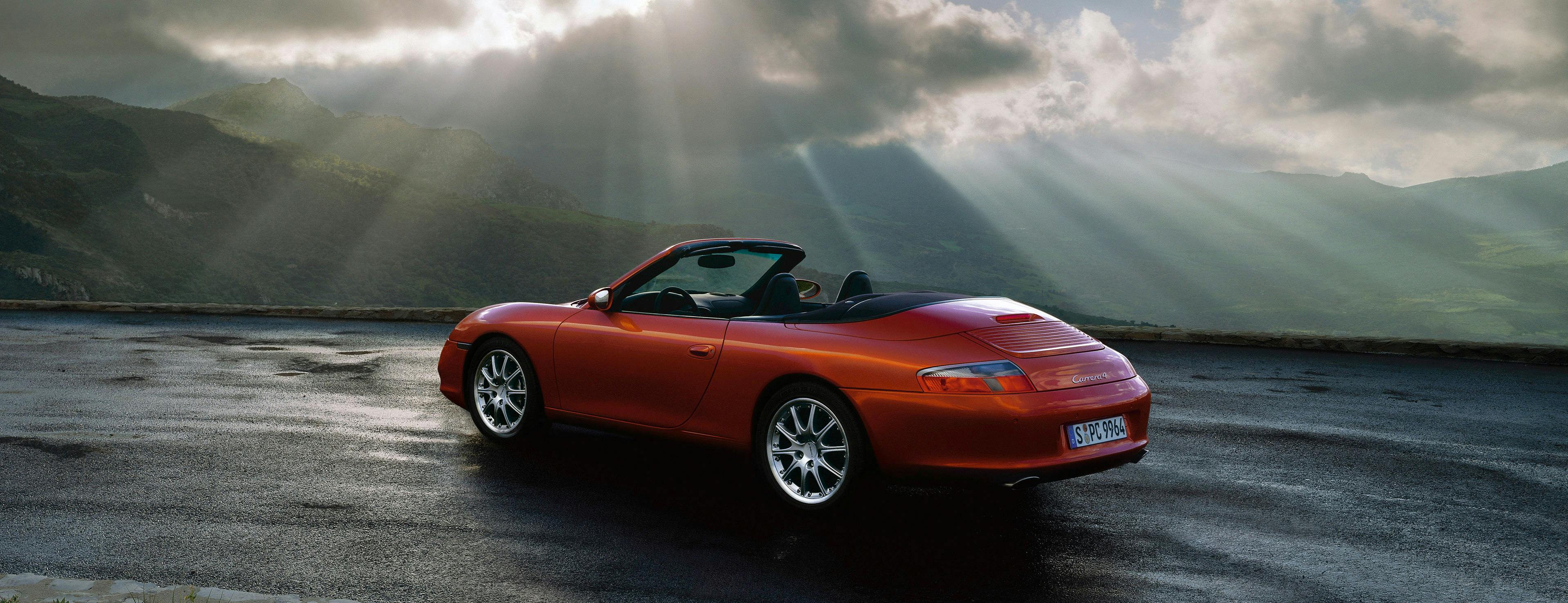 Red Porsche 996 Coupé in motion, clouds, sunbeams, sea.