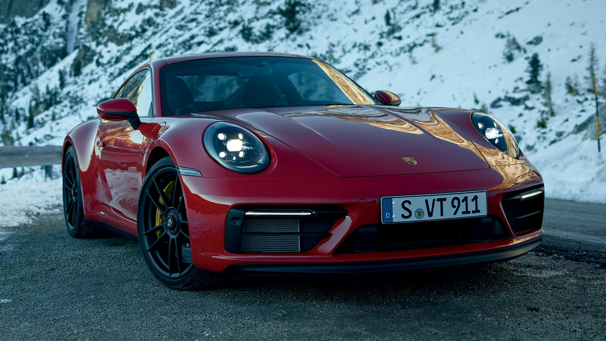 Roter 911 Carrera GTS auf einer winterlichen Bergstraße mit schneebedeckten Bergen im Hintergrund.