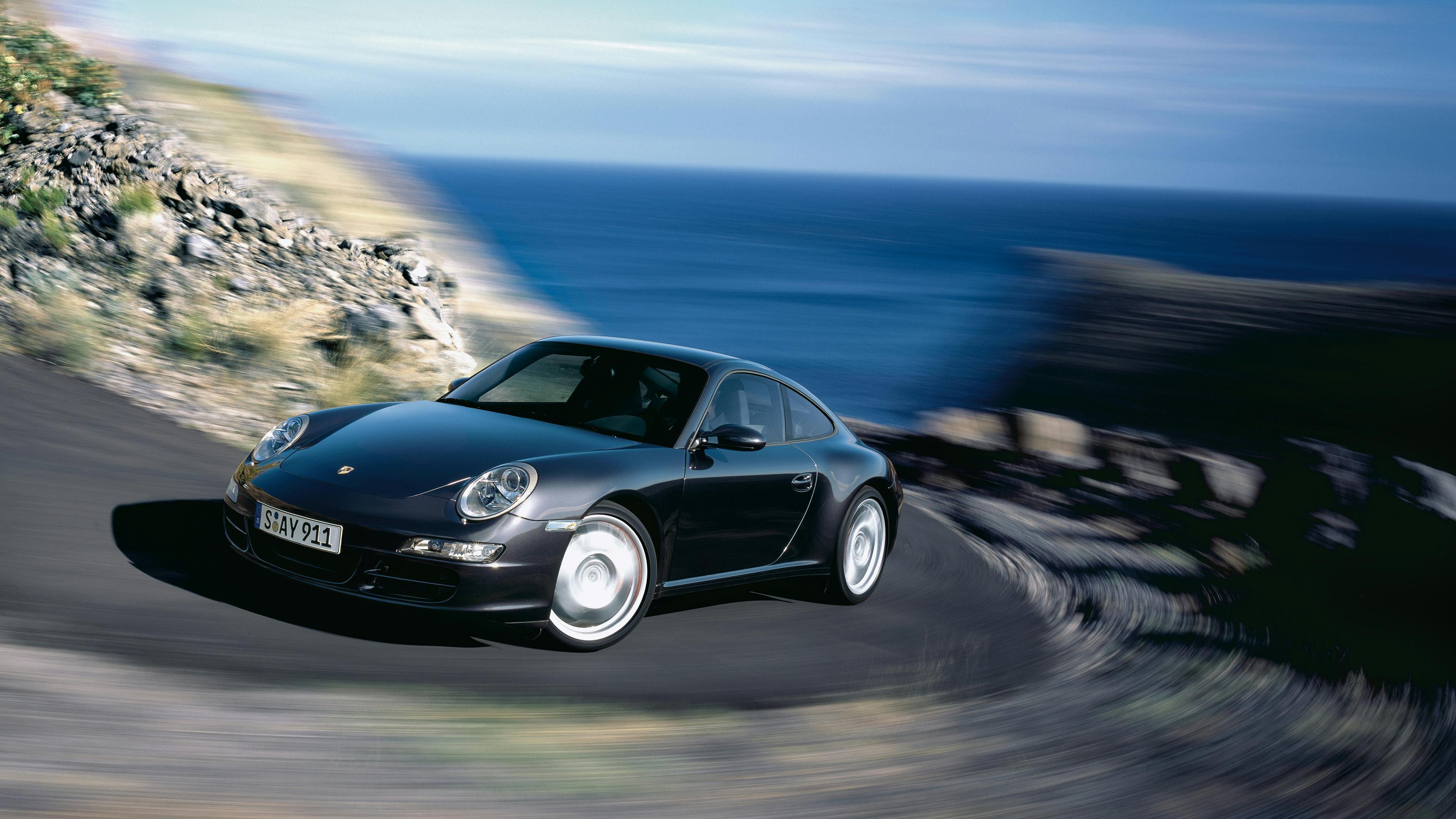 Driving black 911 Carrera 4S Coupé type 997 on a mountain road.