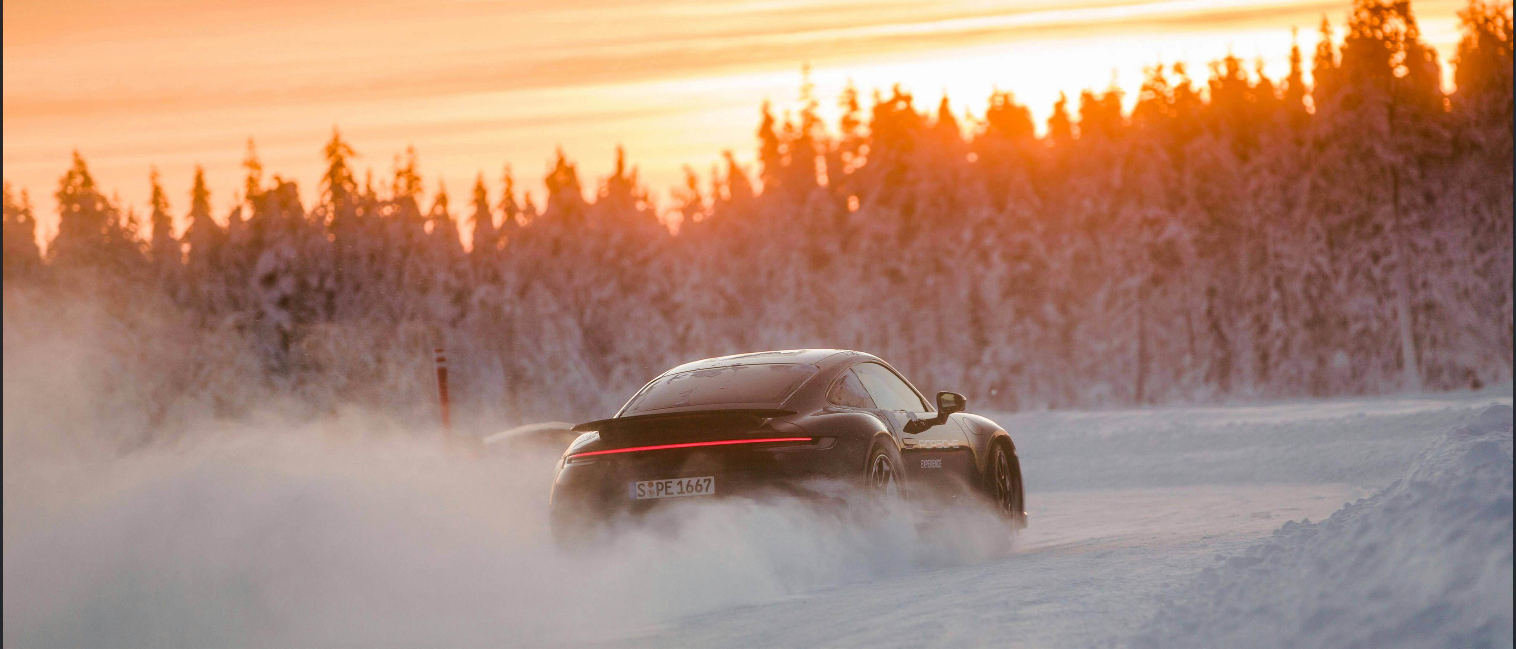 A Porsche car driving along a snow-covered road at sunset.