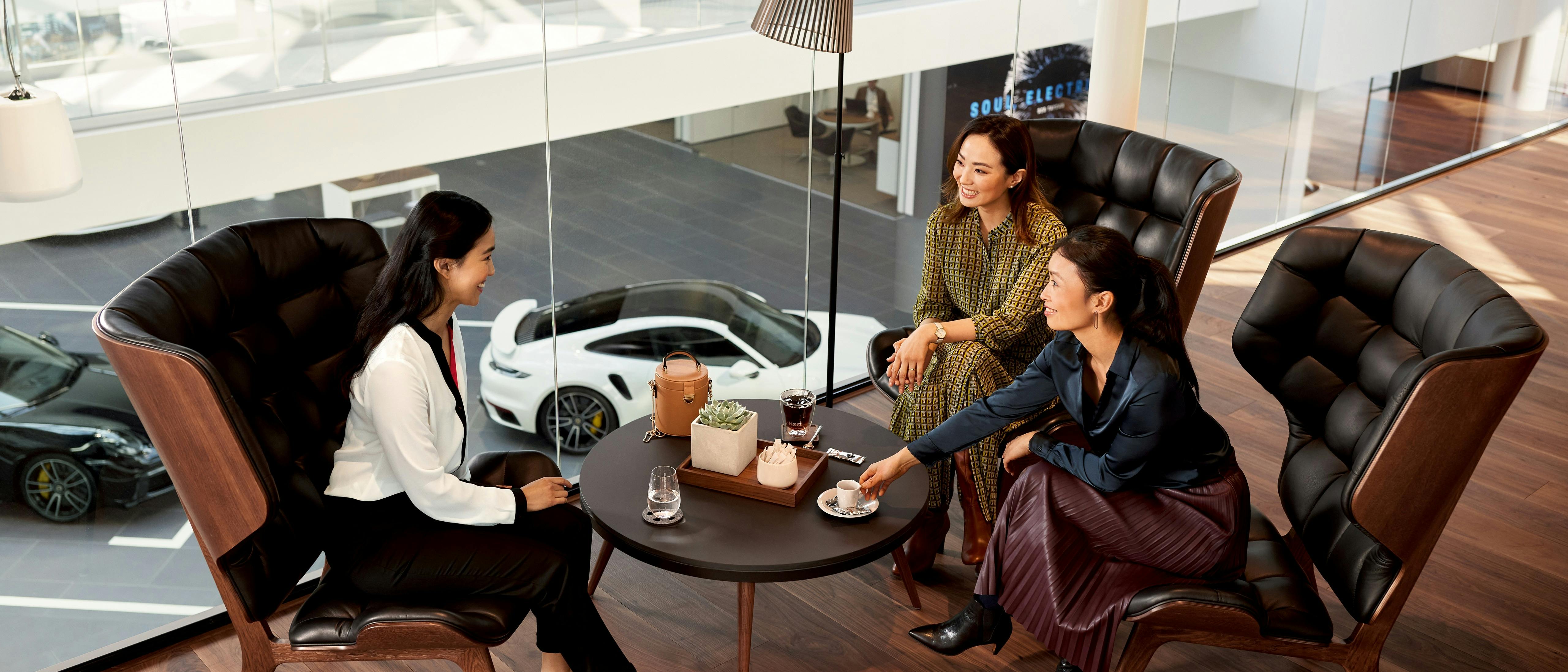 Women enjoying coffee and conversation in a Porsche Centre overlooking the 911.