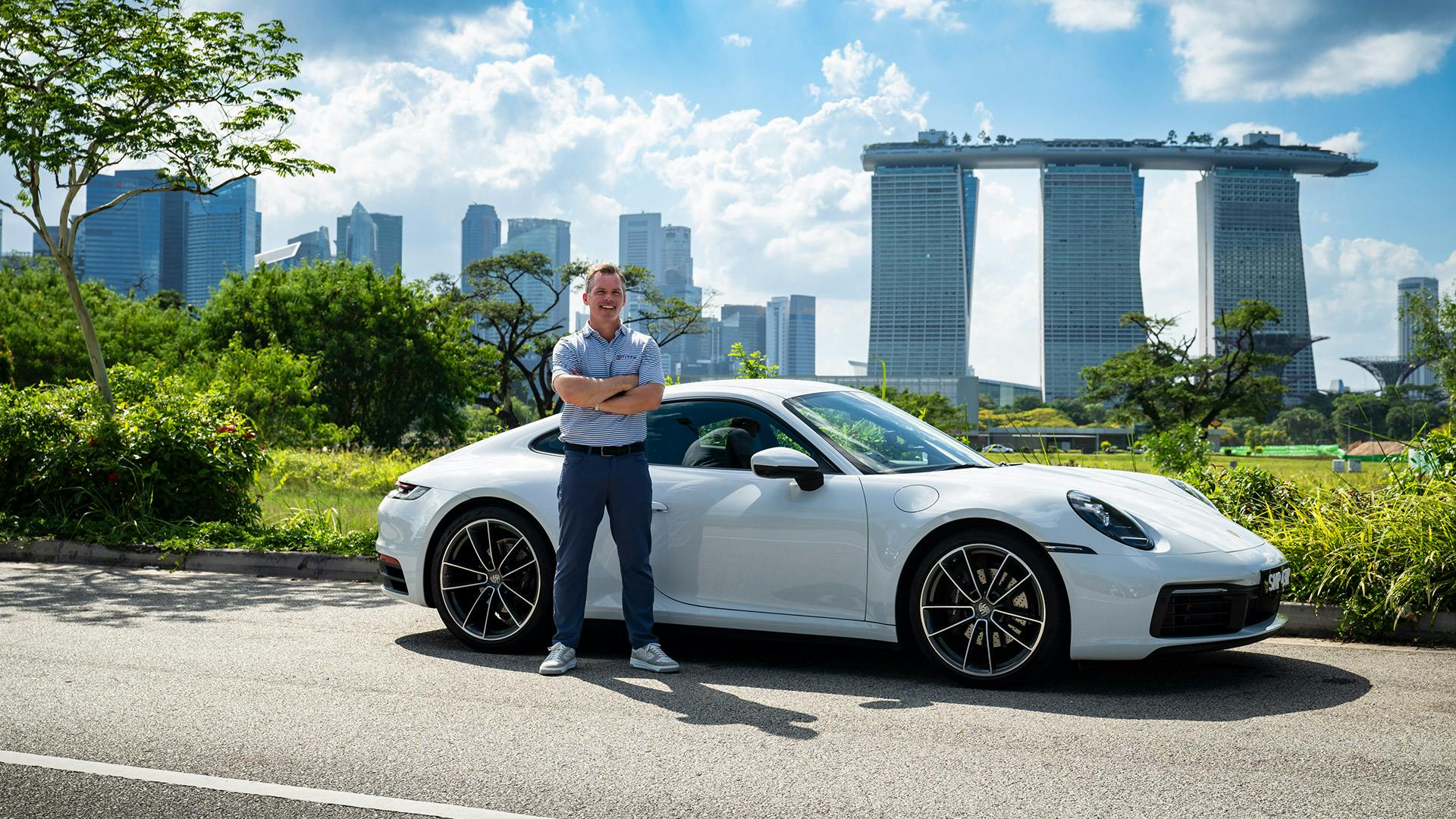 Paul Casey steht vor einem 911 und dem ikonischen Hotel "Marina Bay Sands" in Singapur