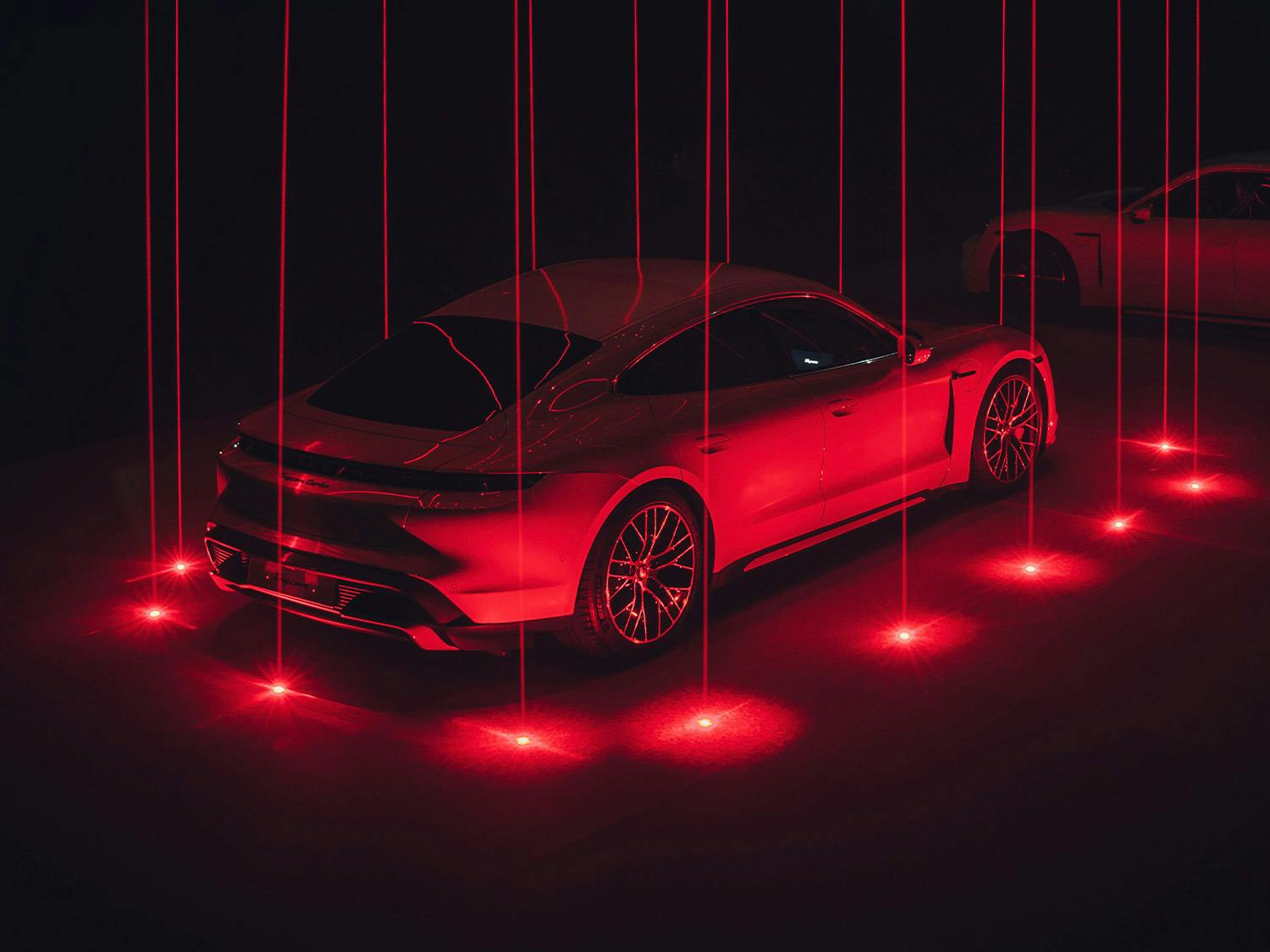 Ein Porsche Taycan wird in einer futistischen Szene mit roten Laserlicht angestrahlt.