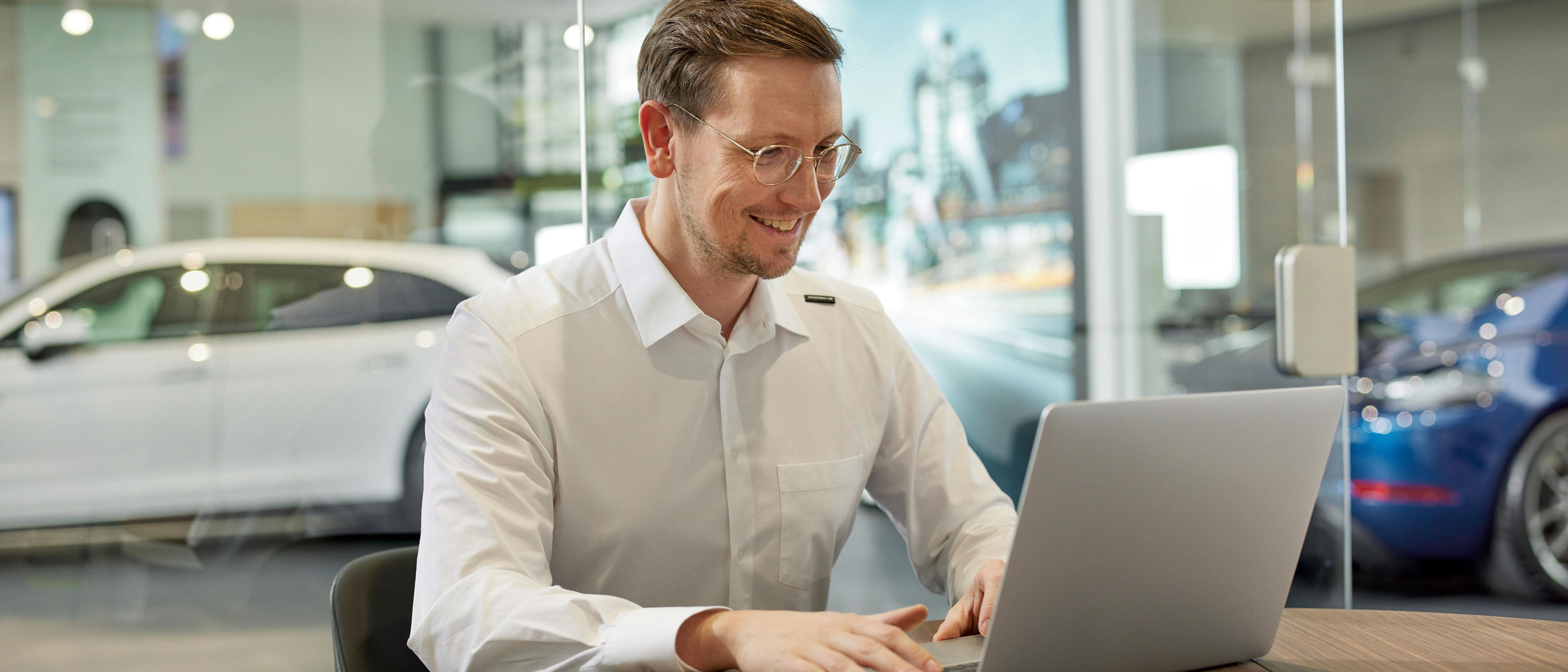Ein Porsche Zentrum Mitarbeiter sitzt und schaut auf ein Laptop.