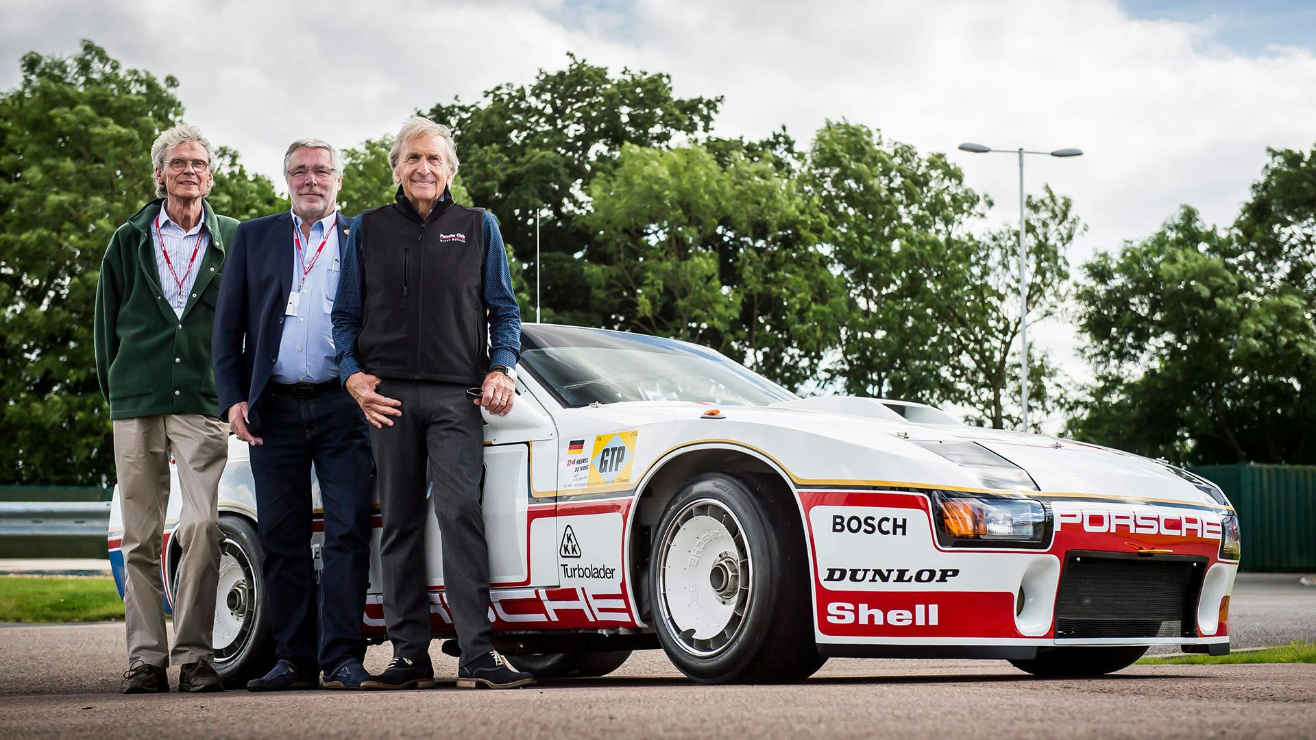 Three men Standing next to fully restored Porsche 924 GTP.