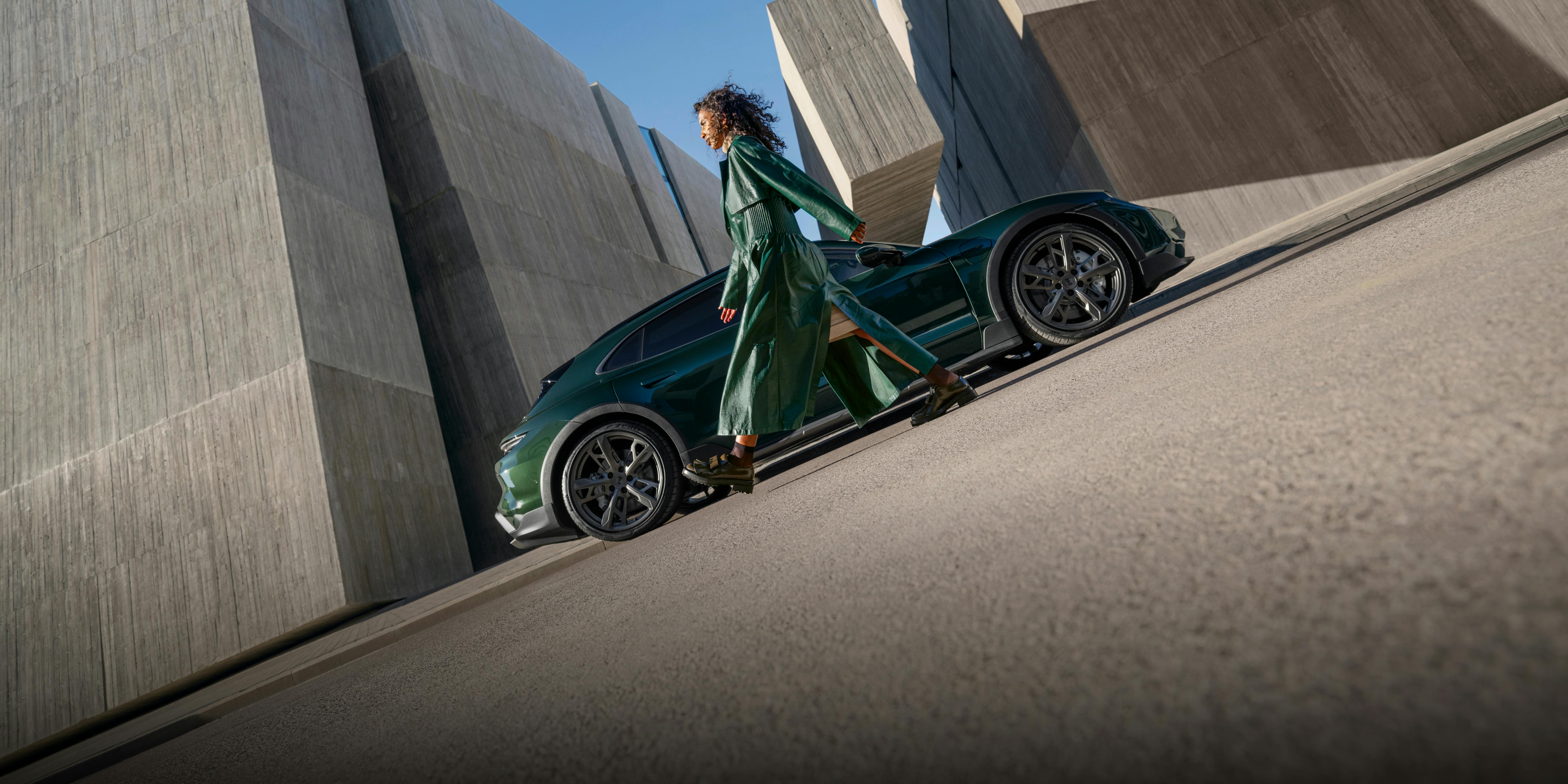 A woman walking past a Porsche Taycan Turbo Cross Turismo, which can be seen from the side.