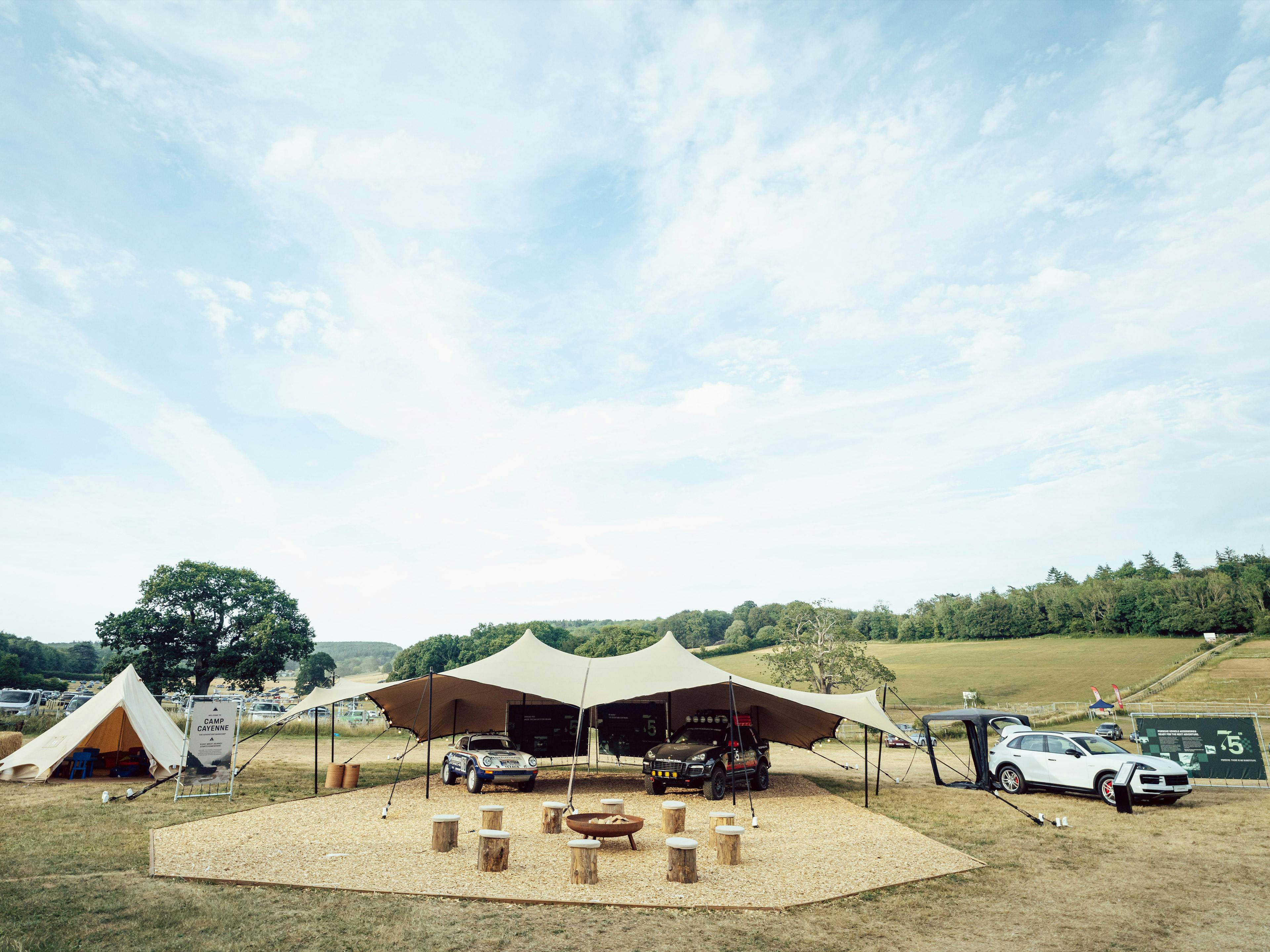 Camp Cayenne tented lounge area with Porsche vehicles in a field.
