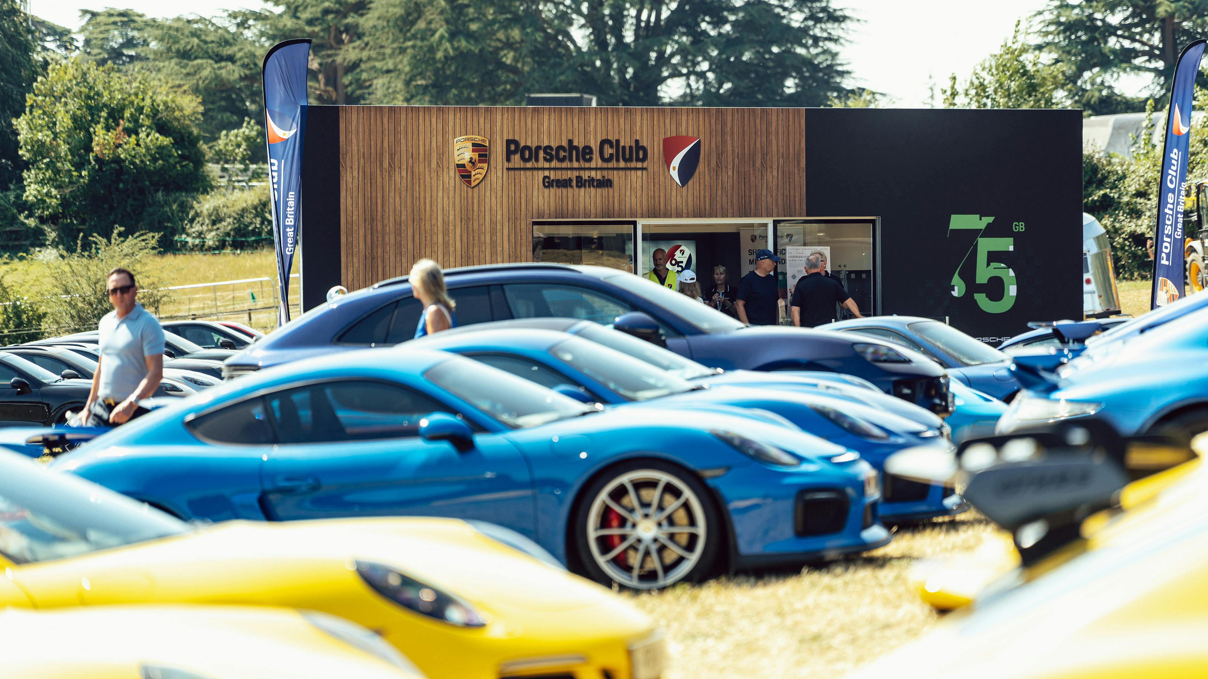 Porsche Club stand at Goodwood Festival of Speed with 75th anniversary signage, surrounded by rows of blue and yellow Porsches.