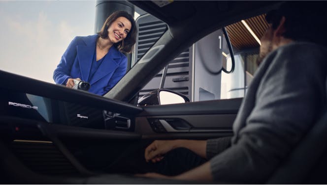 A woman is leaning on a Porsche and looking at her smartphone.