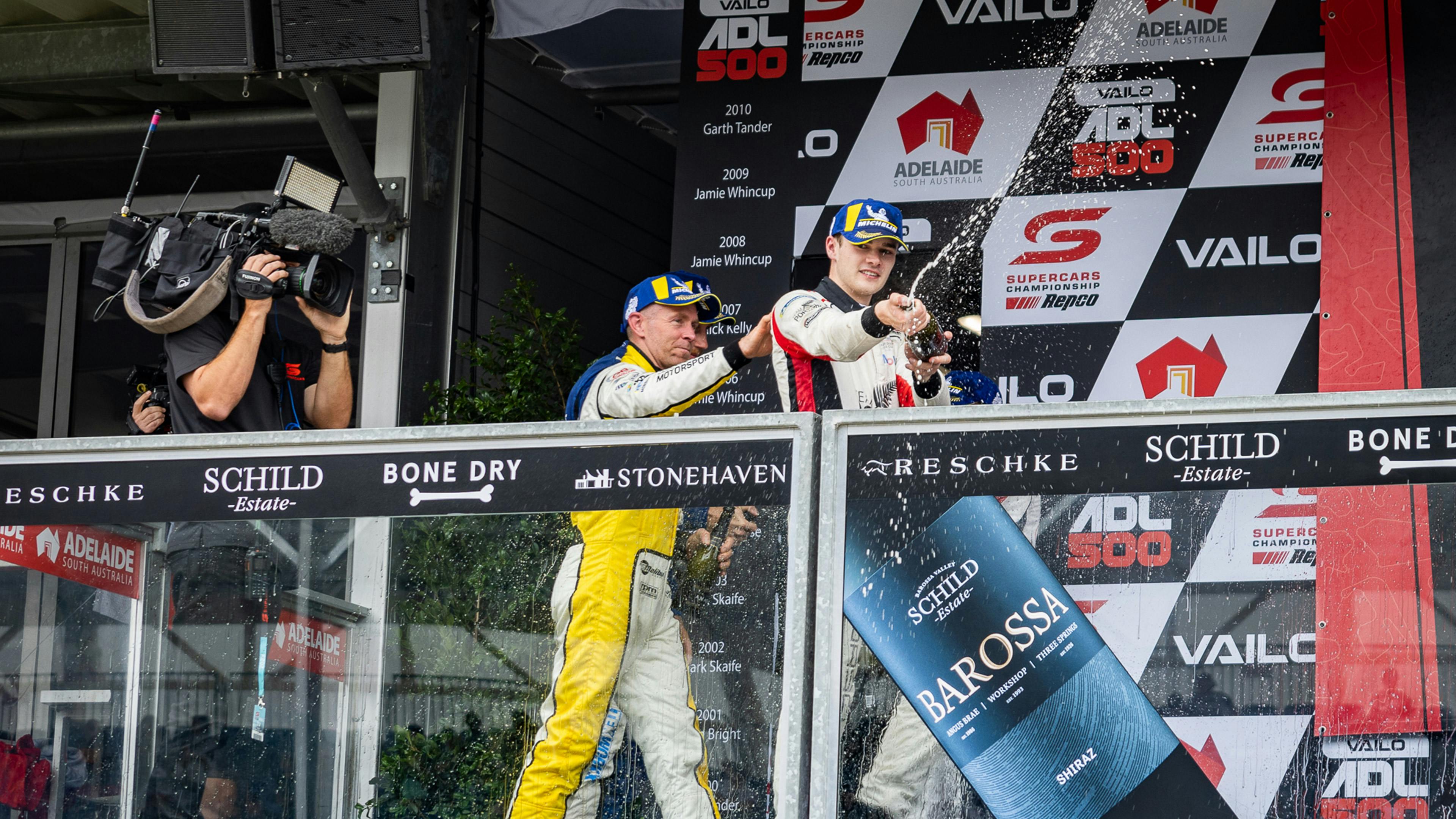 Racing driver spraying champagne down from a grandstand.