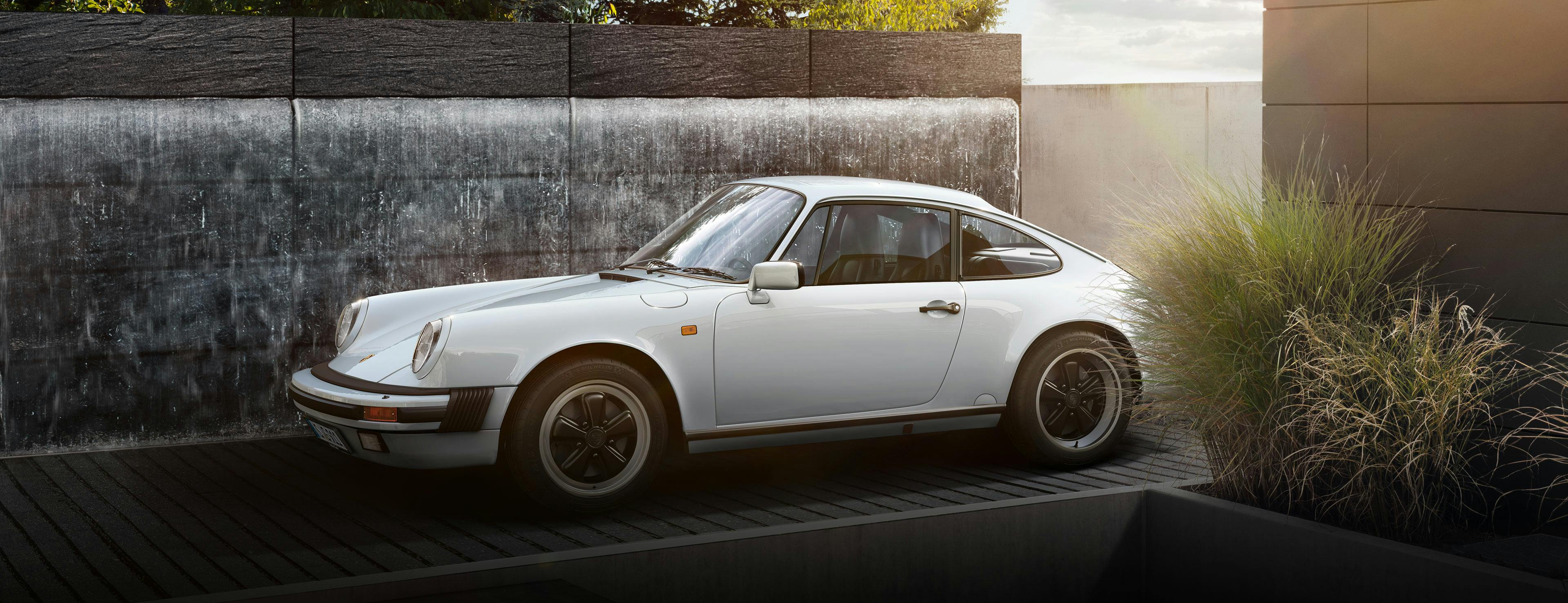 Weißes Porsche Classic 911 G-Modell, vor Haus parkend.