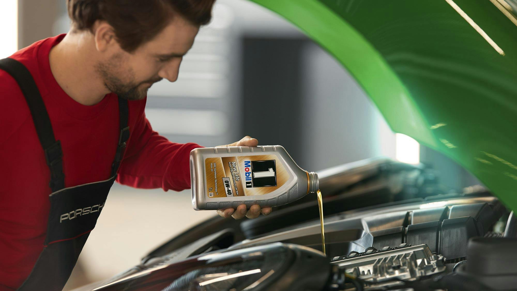 Porsche mechanic pouring oil into a car engine.