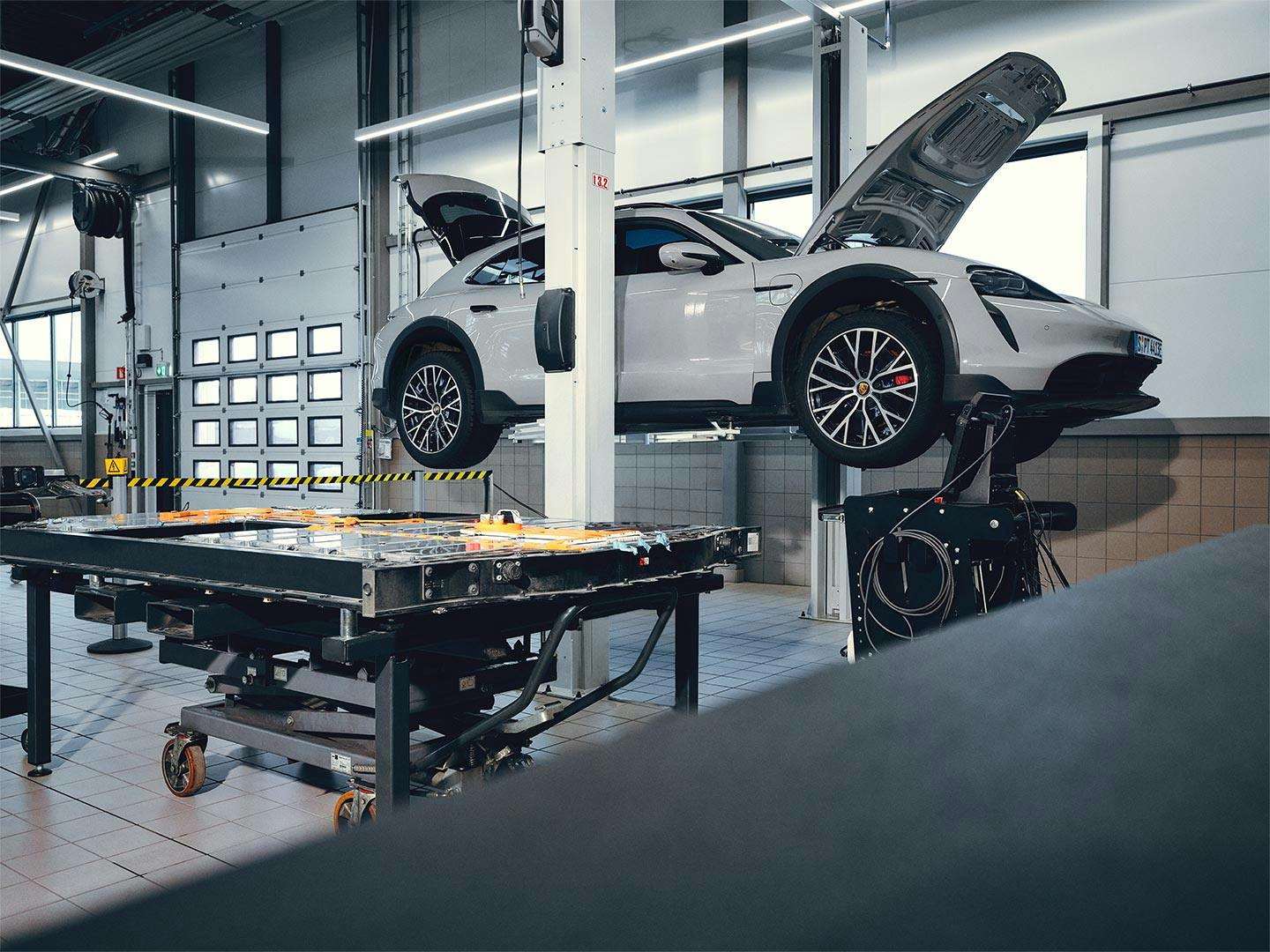 A white Porsche Taycan is being repaired on a lifting platform in the workshop.