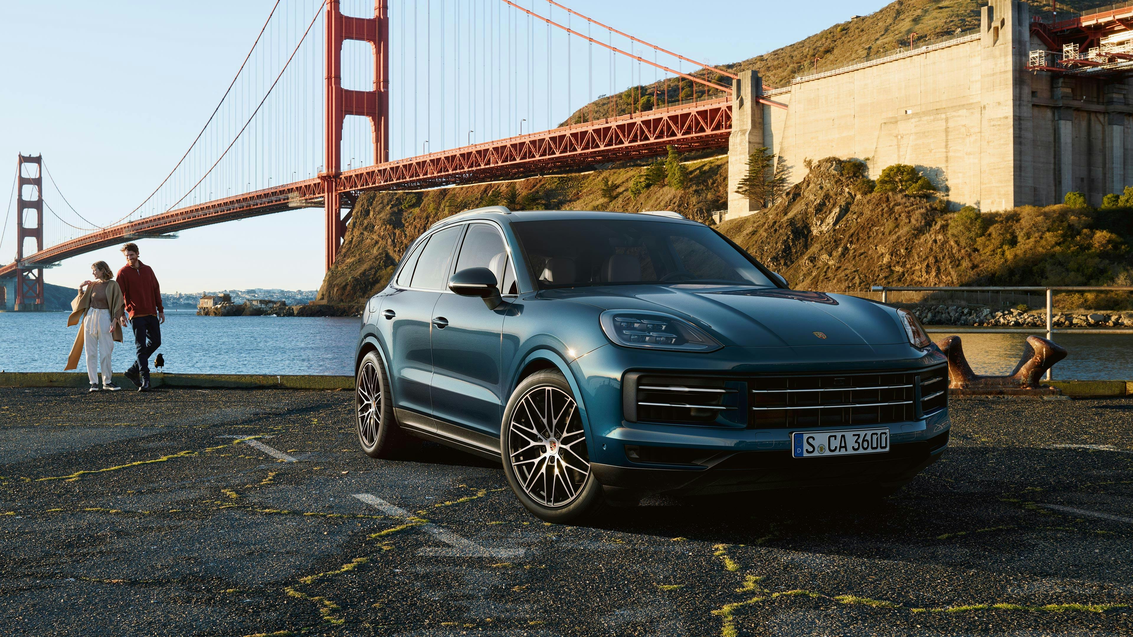 Porsche Cayenne azul estacionado junto al mar, con el puente Golden Gate de San Francisco al fondo.