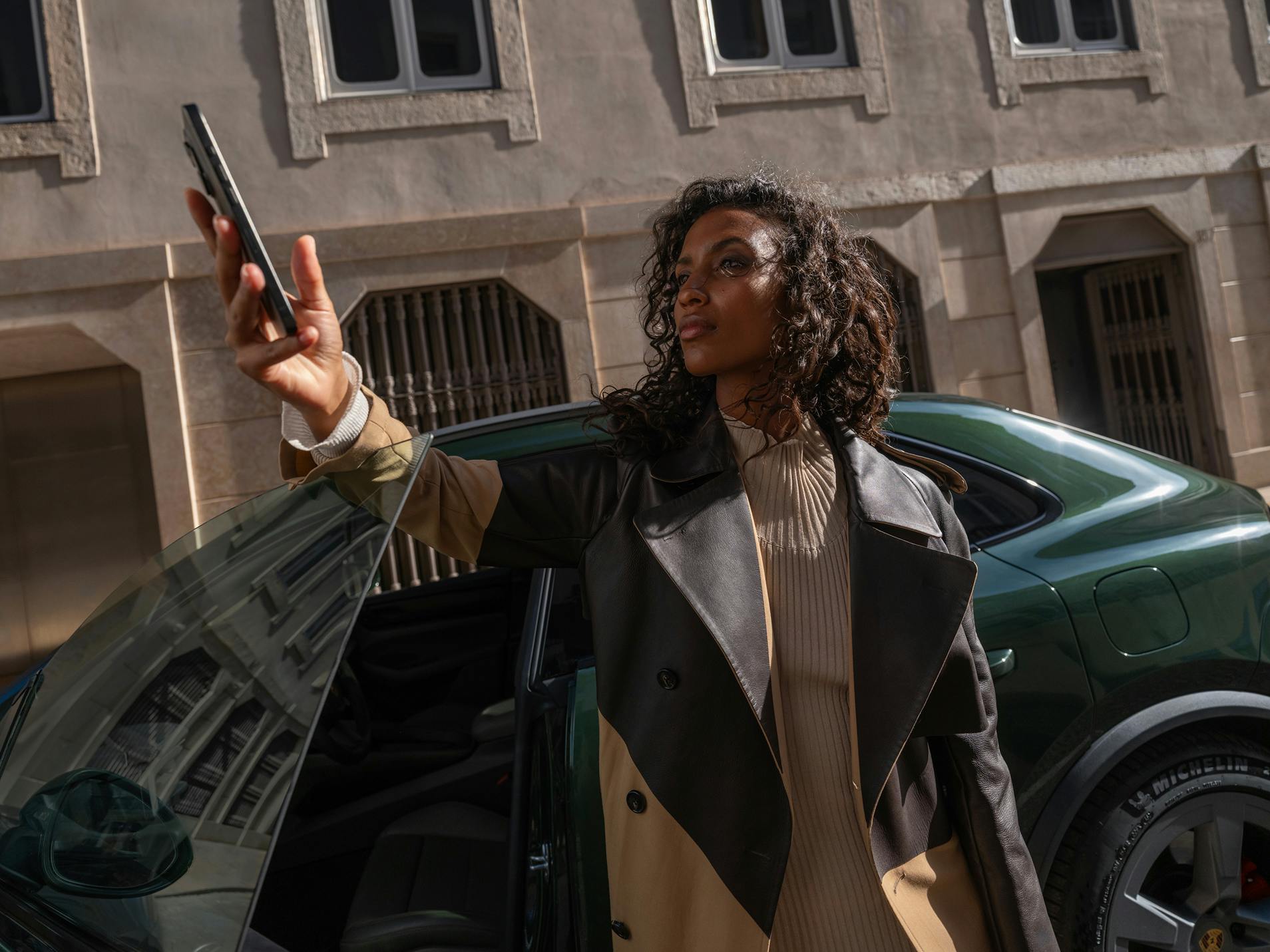 A woman standing in the door of a Porsche Macan 4S and looking at her smartphone.