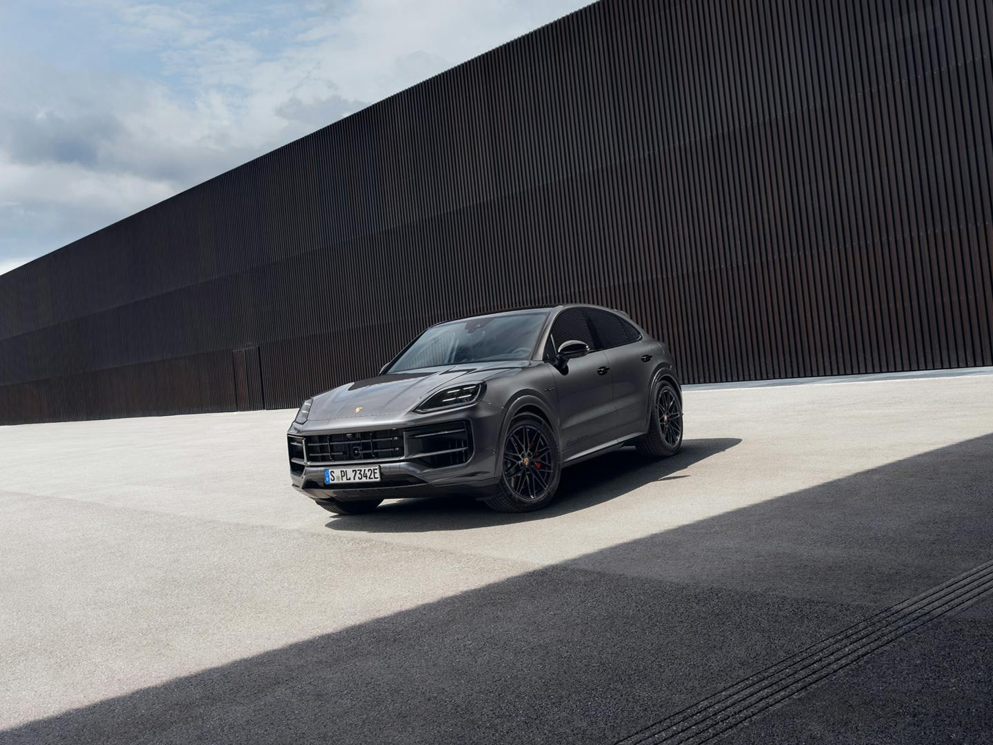 The Cayenne S E-Hybrid Coupé Black Edition parked outside a modern building that is made up of dark textured material and also glass.