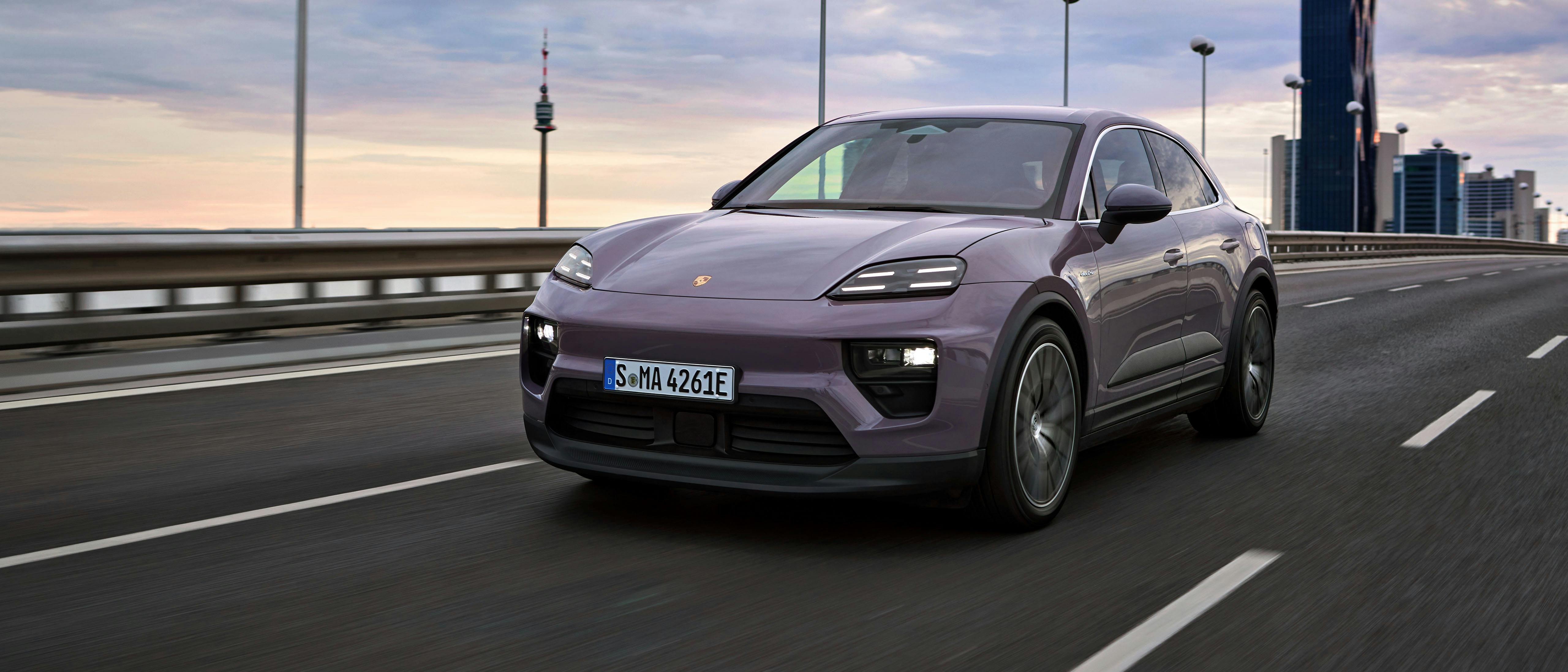 A Macan 4 Electric in Provence driving across a long road, with tall buildings in the background.
