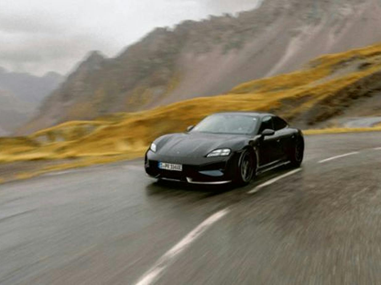 Um Porsche Taycan a circular numa estrada molhada atravessando uma paisagem montanhosa.