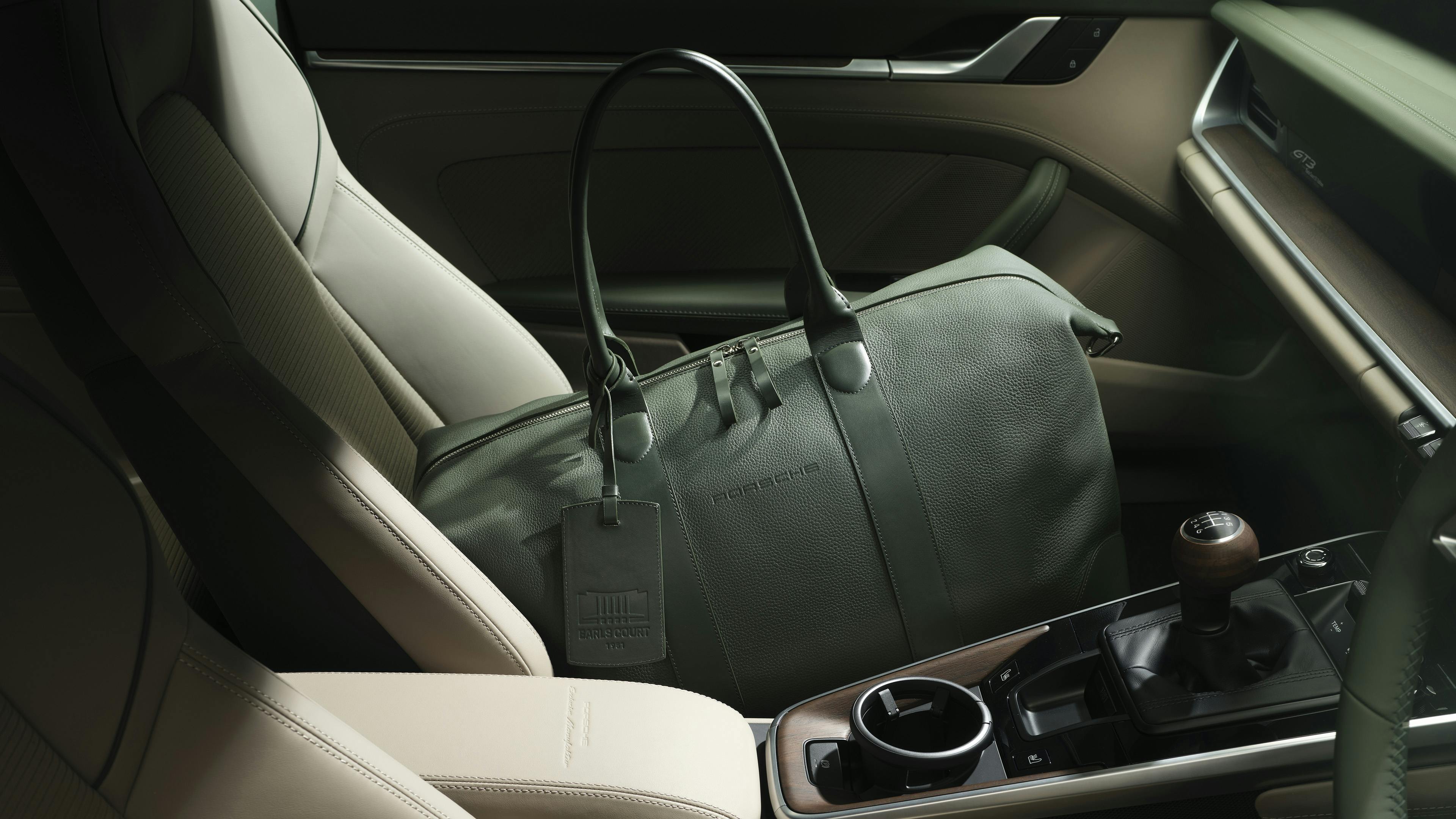 A green leather holdall resting on the cream leather rear seats of a Porsche 911 interior.​