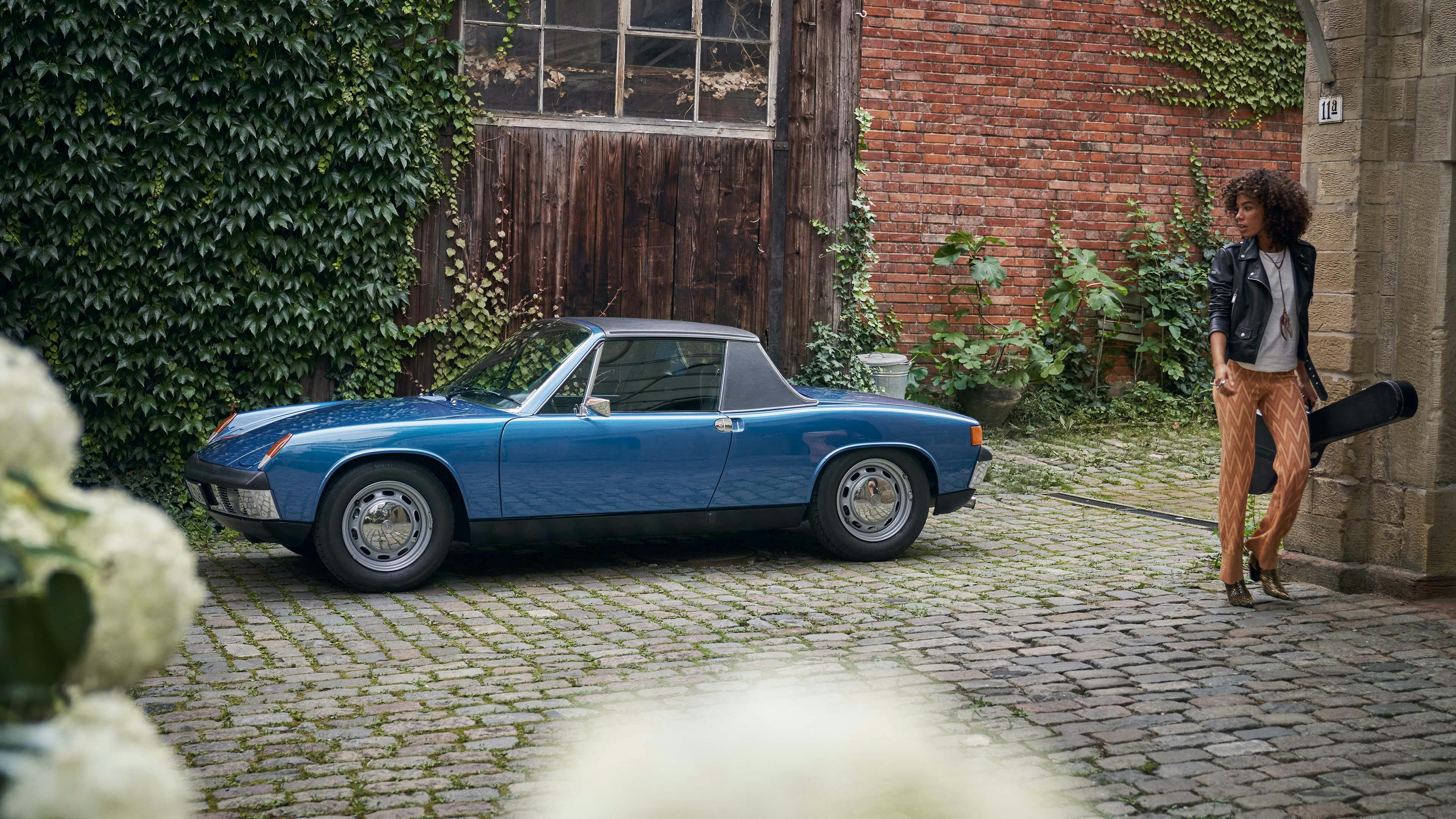 Porsche 914 geparkeerd in steegje met een vrouw die wegloopt bij de auto met haar instrument.
