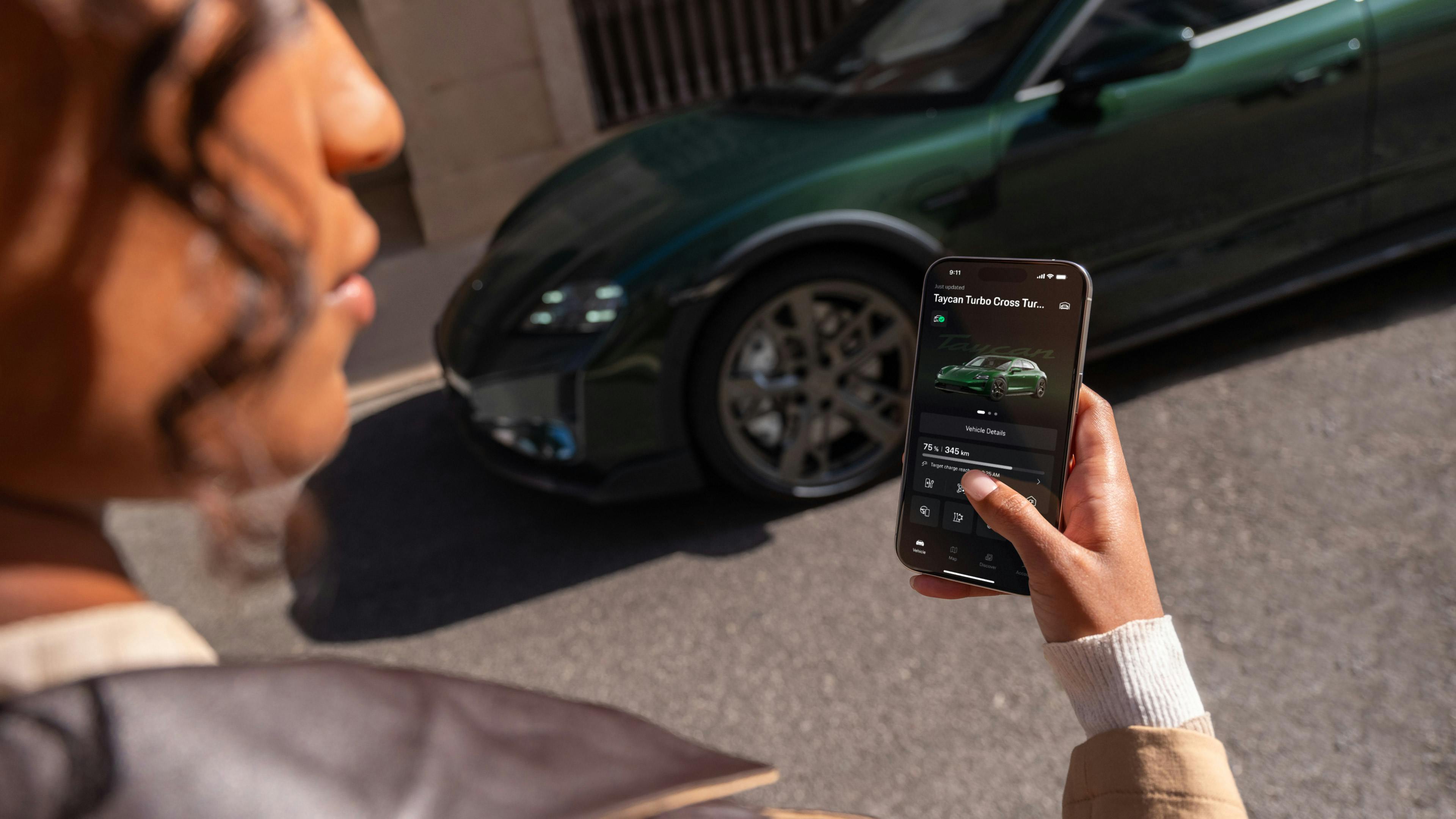 A woman standing in front of a green Porsche Taycan and using her phone to change the settings on her vehicle.