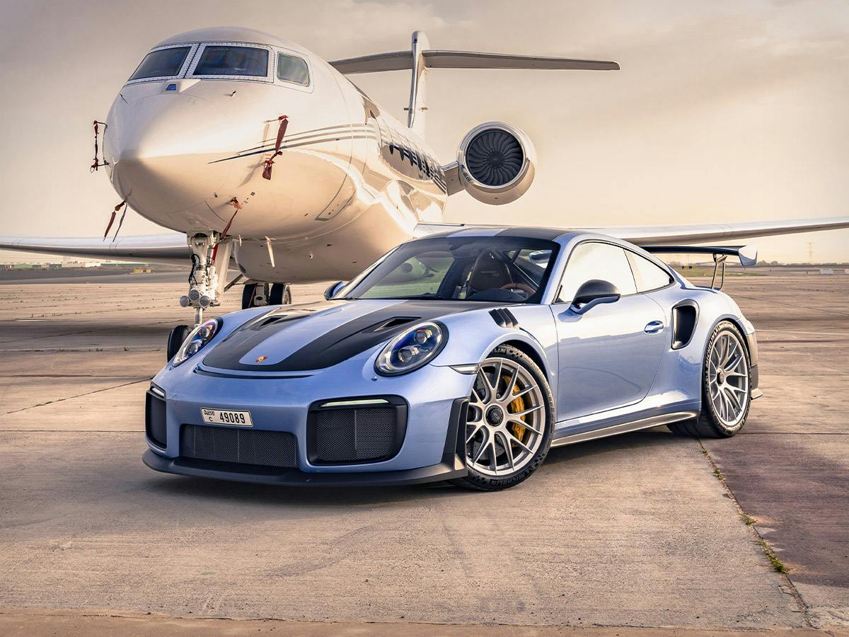 A 911 GT2 RS coloured in Geminimetallic in the left front of a small airplane on the tarmac.