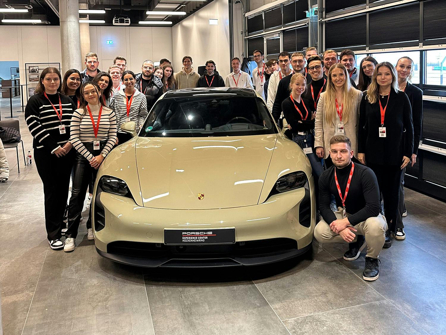 Eine Gruppe von jungen Menschen ist um einen weißen Porsche Taycan versammelt.