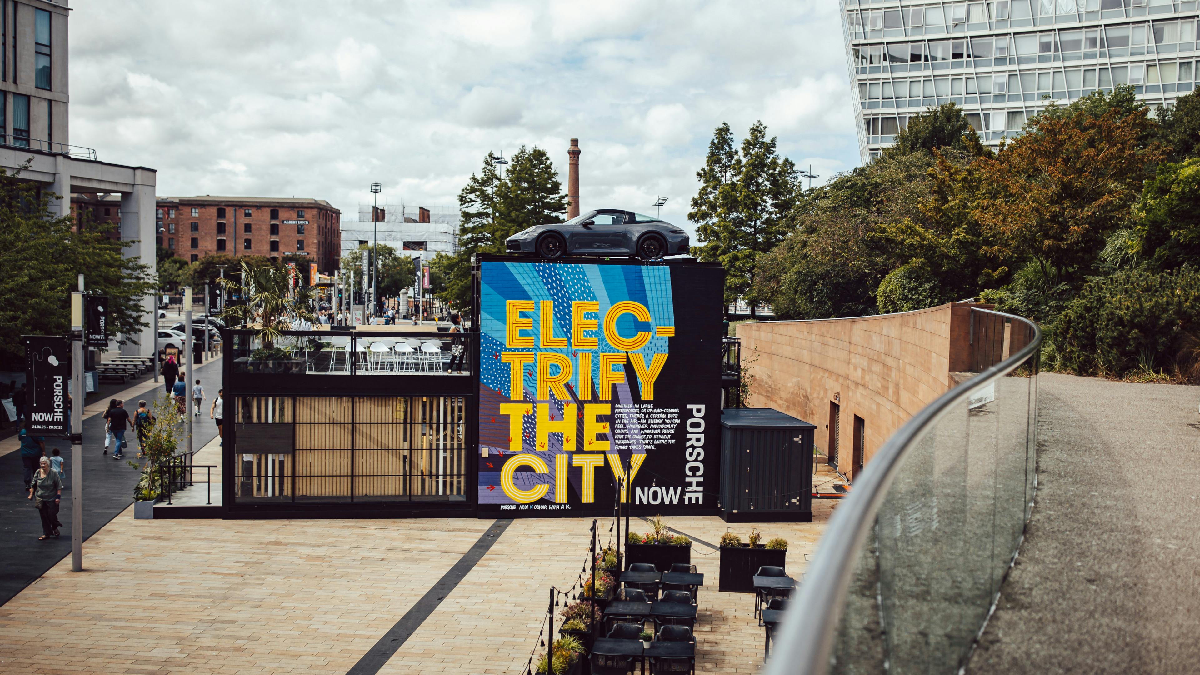 A higher view the Porsche Now Liverpool pop up with “Electrify the City” on the side, with a sports car displayed on the roof.