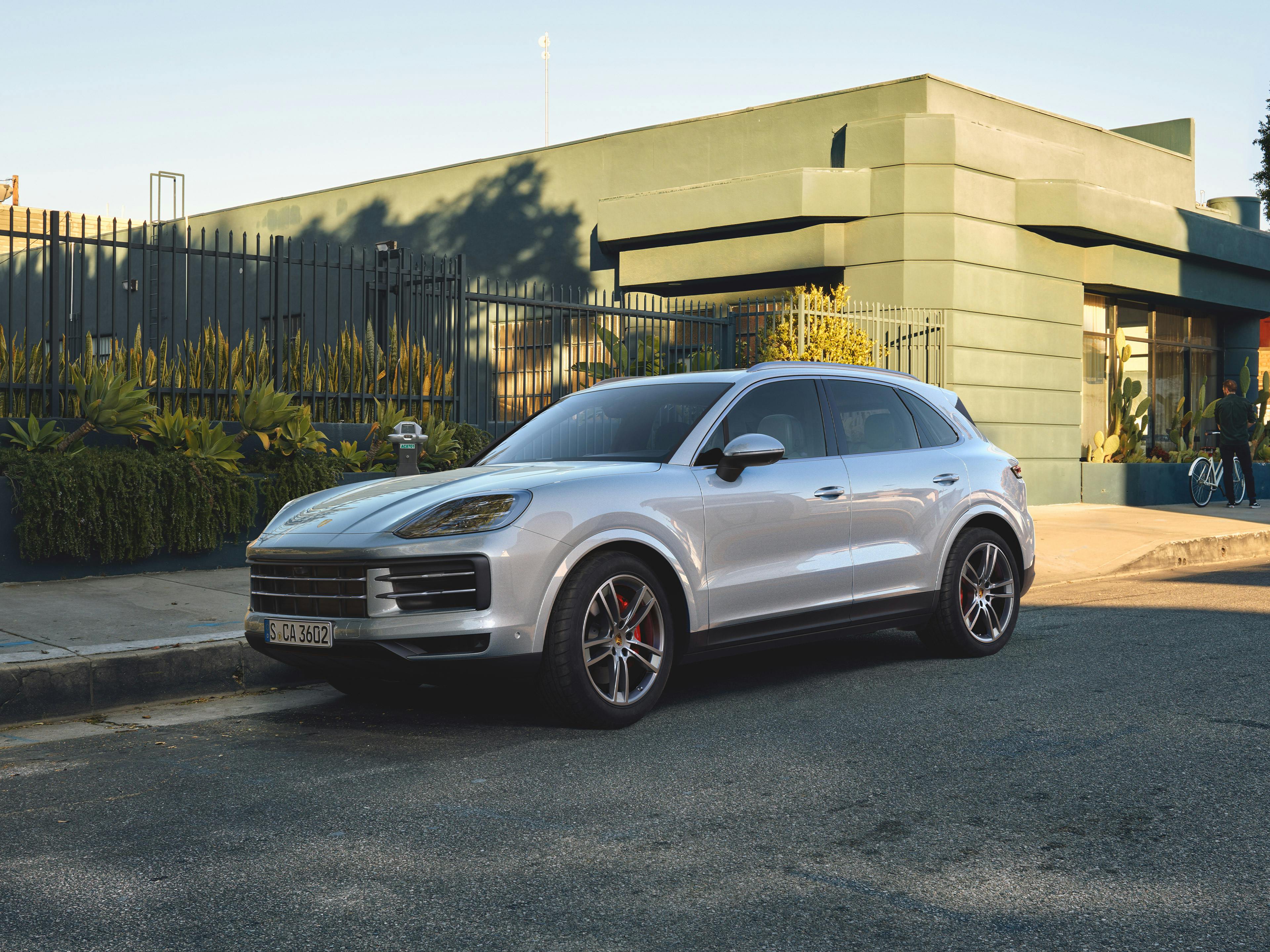 Ein silbener Cayenne parkt nah am Bürgersteig in einer städtischen Umgebung.
