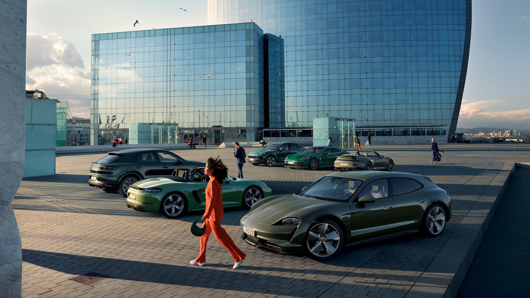 Une femme passe devant des Porsche alignées de différentes couleurs.
