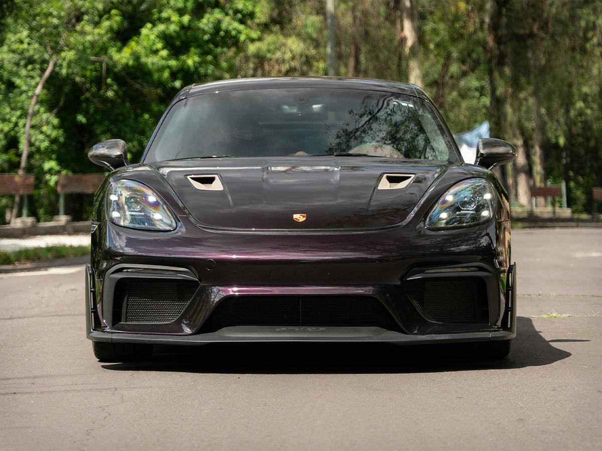 718 GT4 RS in Paint to Sample colour Amethystmetallic with Whitegoldmetallic painted elements, shown from the front on a tree-lined street.