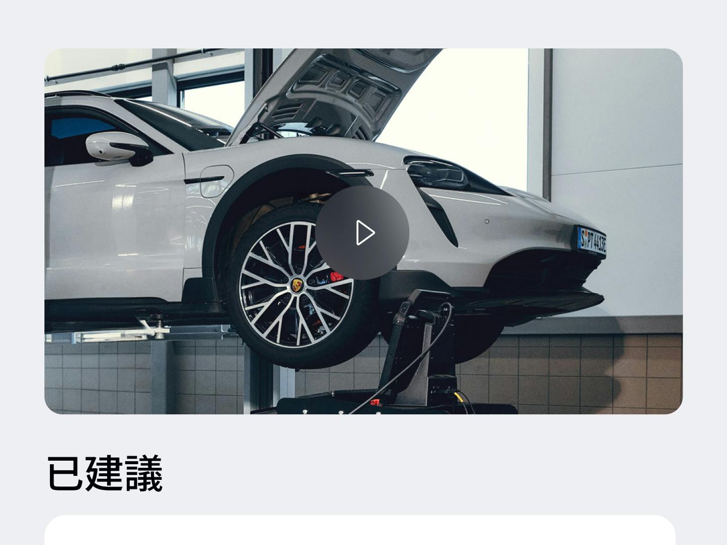 應用程式畫面顯示淺灰色保時捷置於舉升機上，引擎蓋開啟，下方顯示影片播放按鈕與推薦文字。