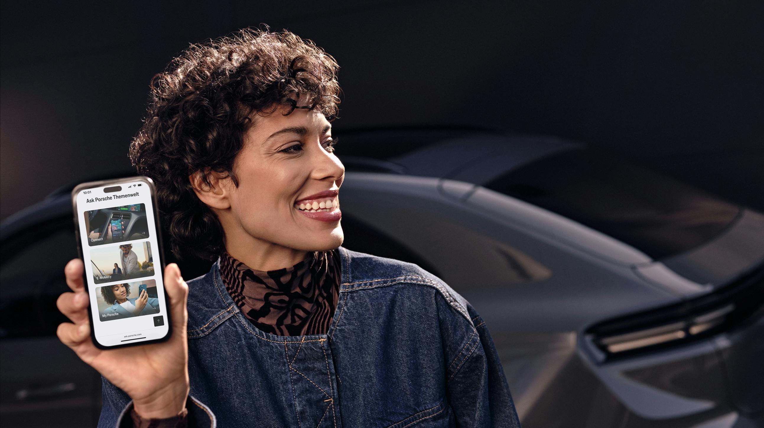 A woman smiling and holding her smartphone up to the camera.