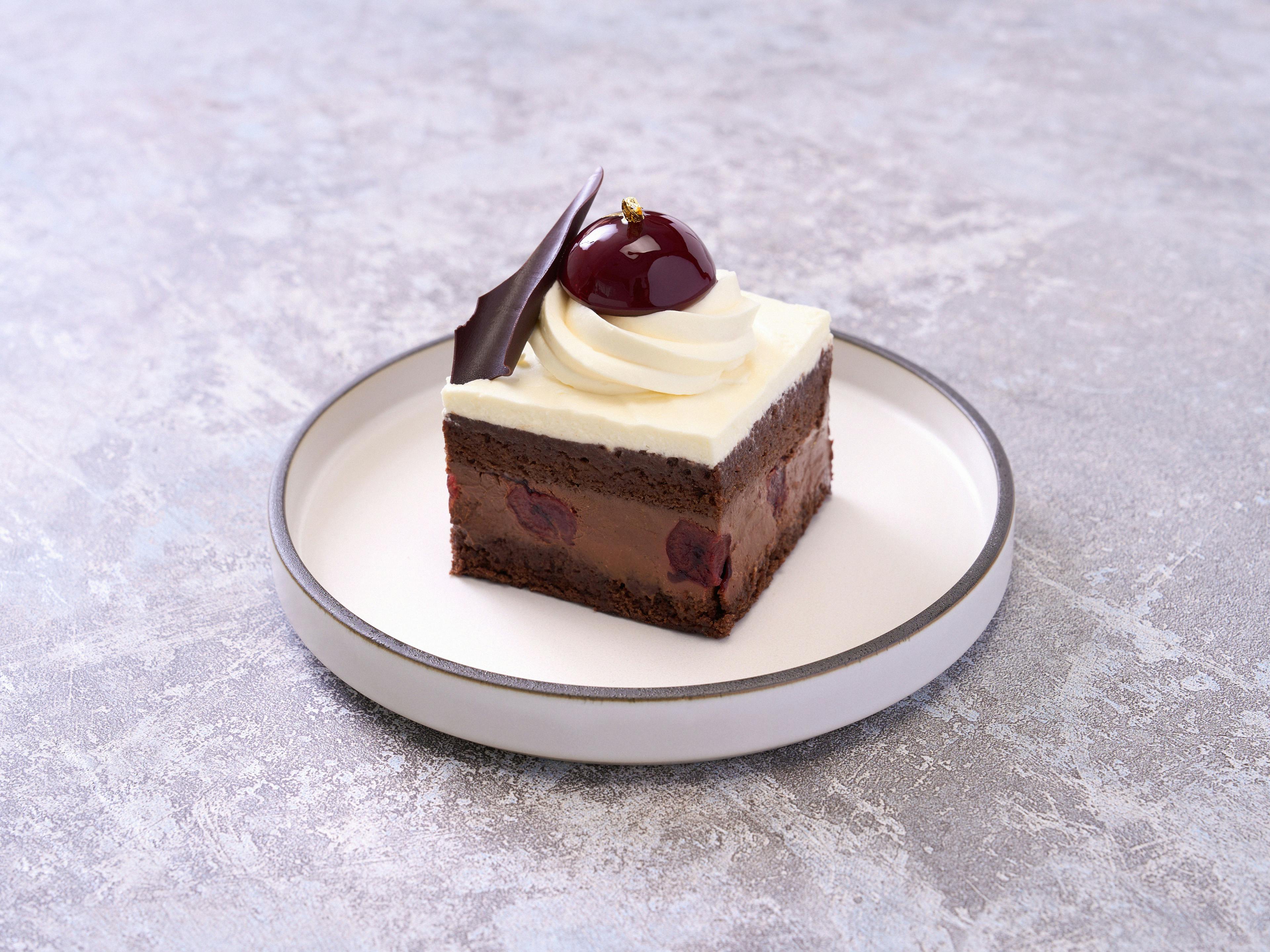 Black Forest cake dessert with whipped cream, cherry and chocolate decor, served on a white plate.