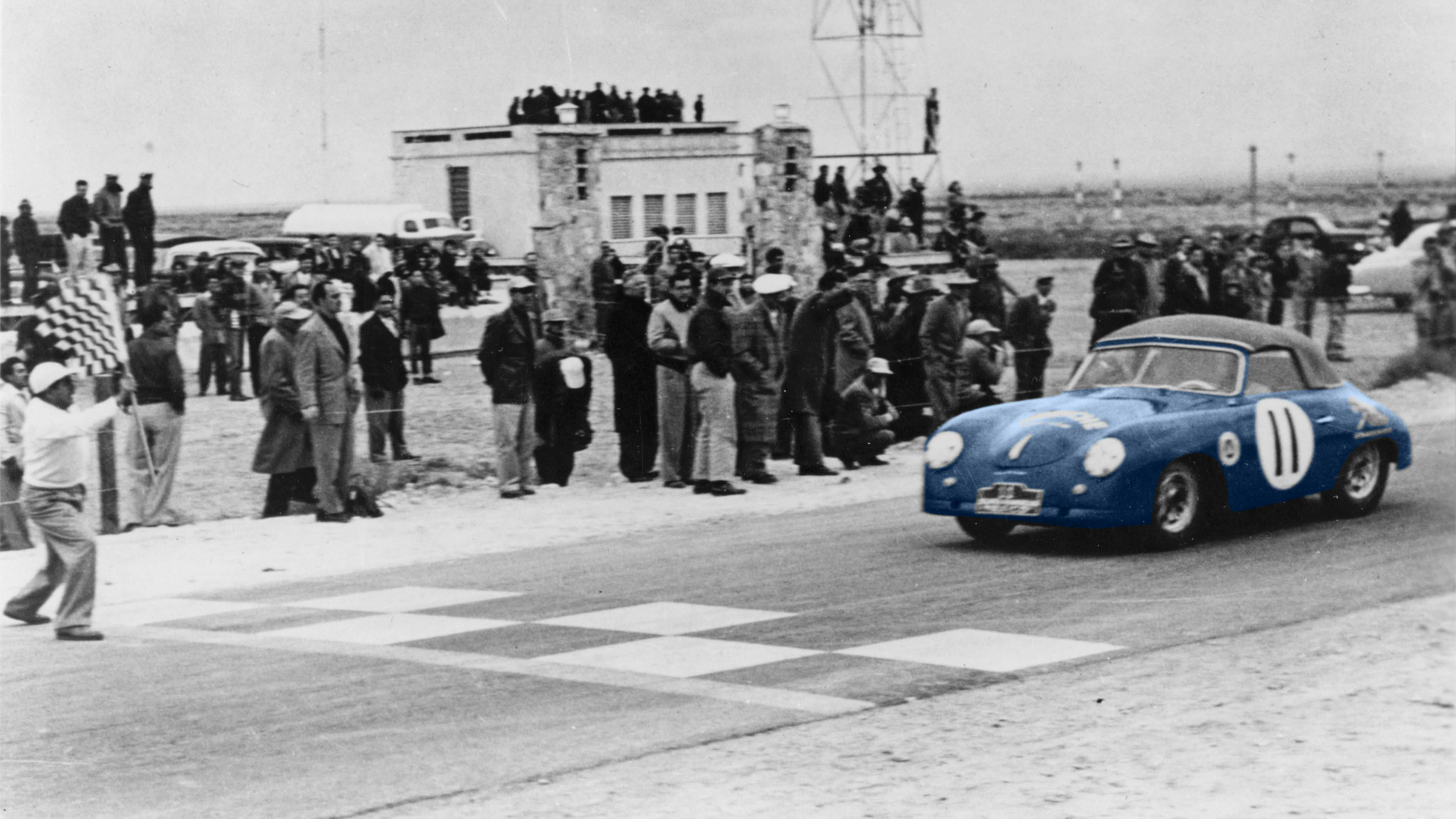 A group of people observing a Porsche 356 S Cabriolet just before crossing the finish line, circa 1952.