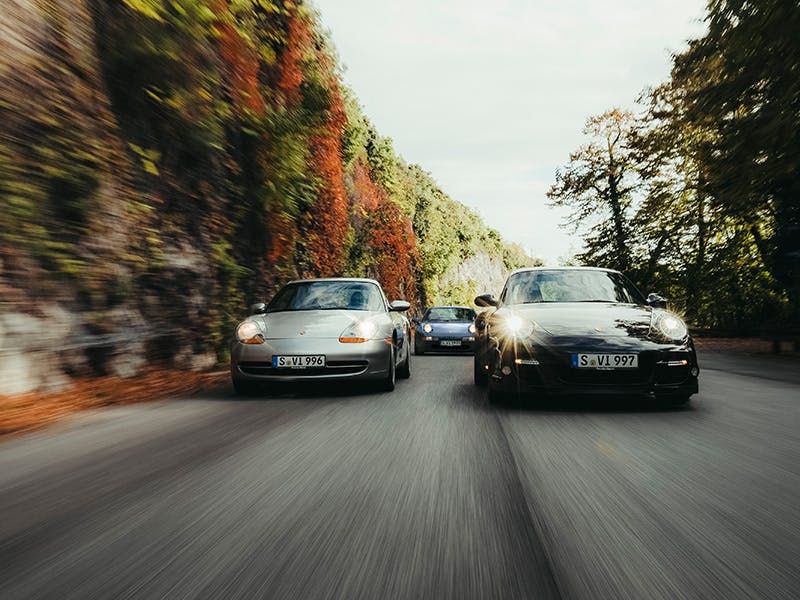 Three driving classic Porsche from the front on a road.