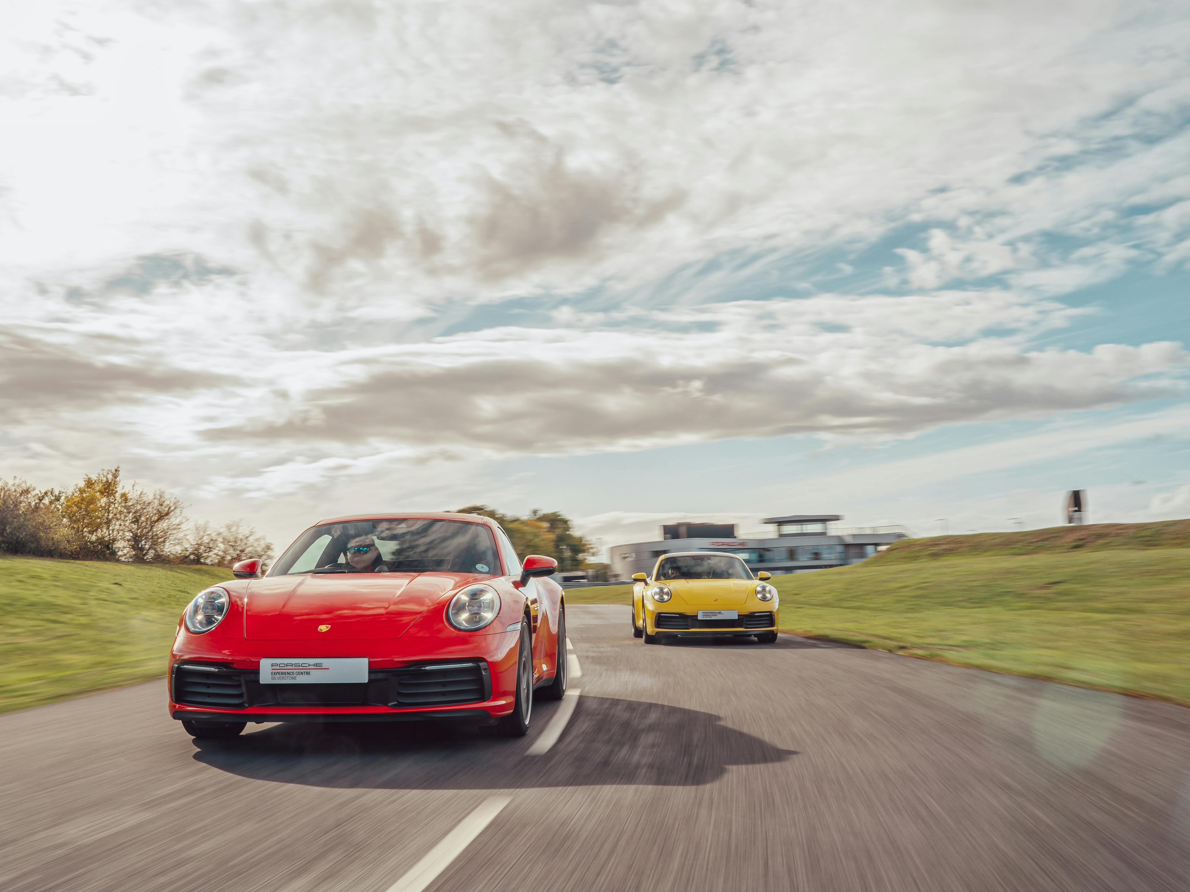 A red Porsche 911 Carrera driving on the racetrack at Porsche Experience Centre Silverstone with a yellow 911 Carrera close behind.