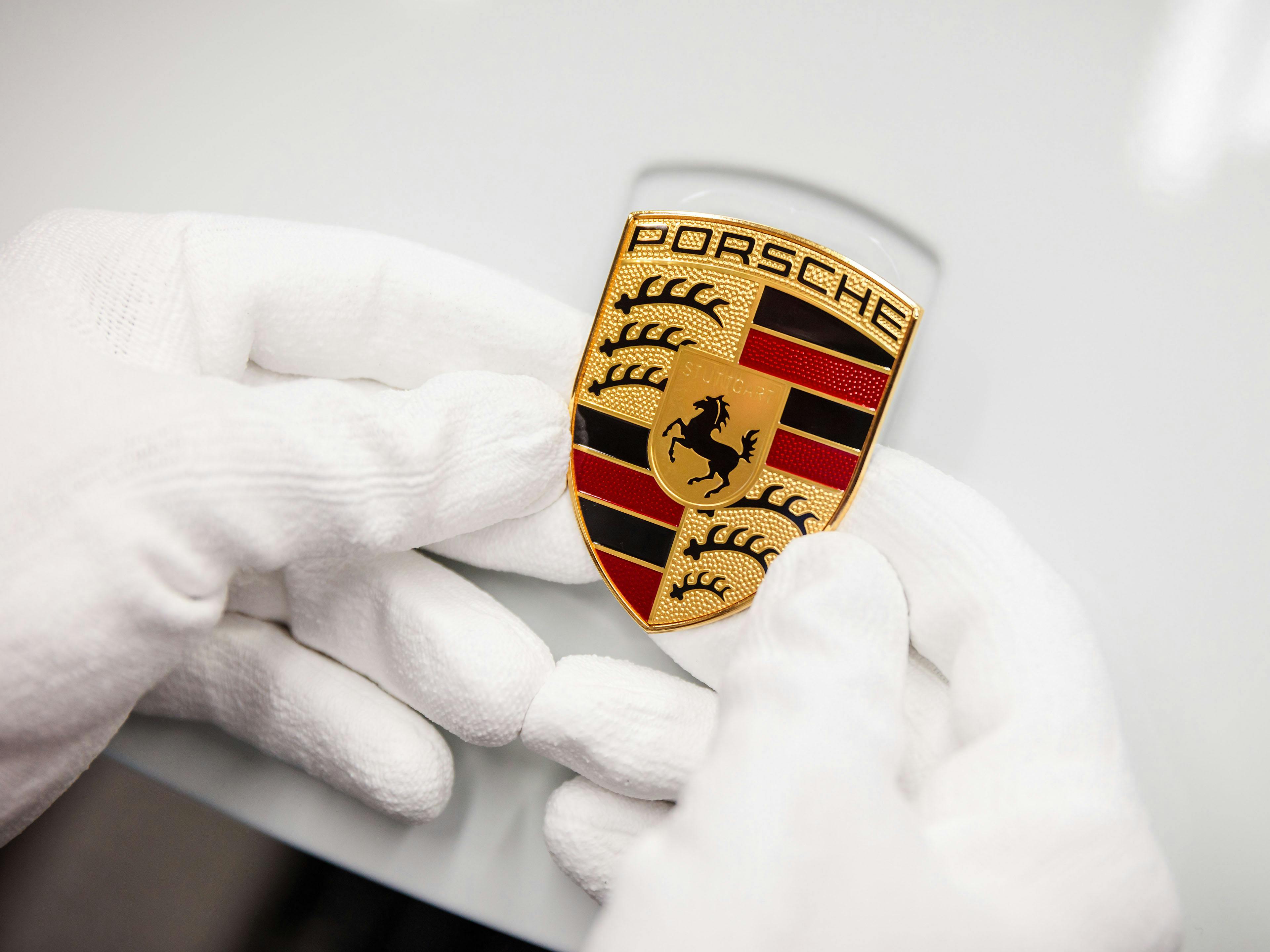 Hände in weißen Handschuhen halten das Porsche Wappen.