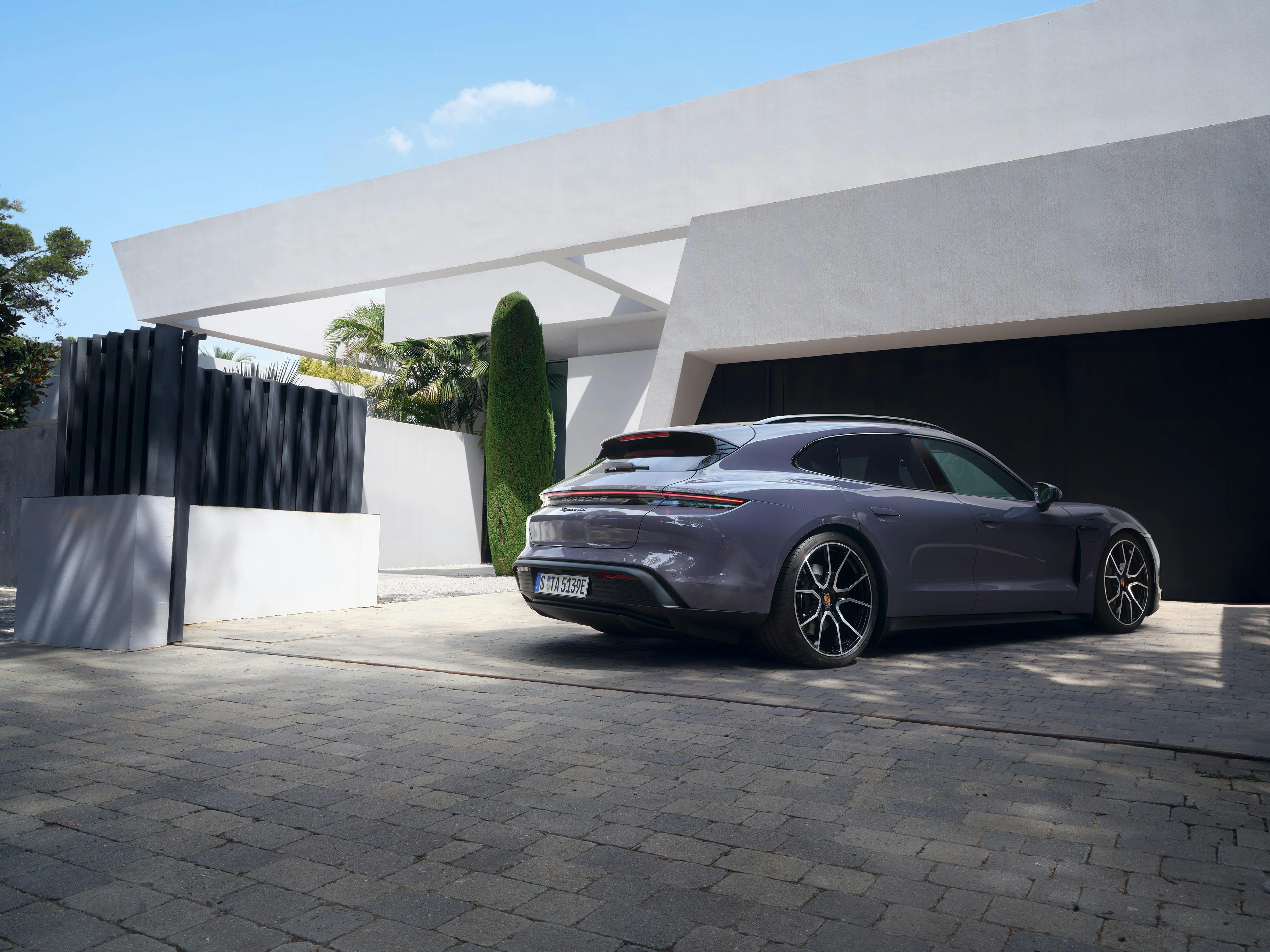 A Porsche Taycan Sports Turismo parked outside a modern home.
