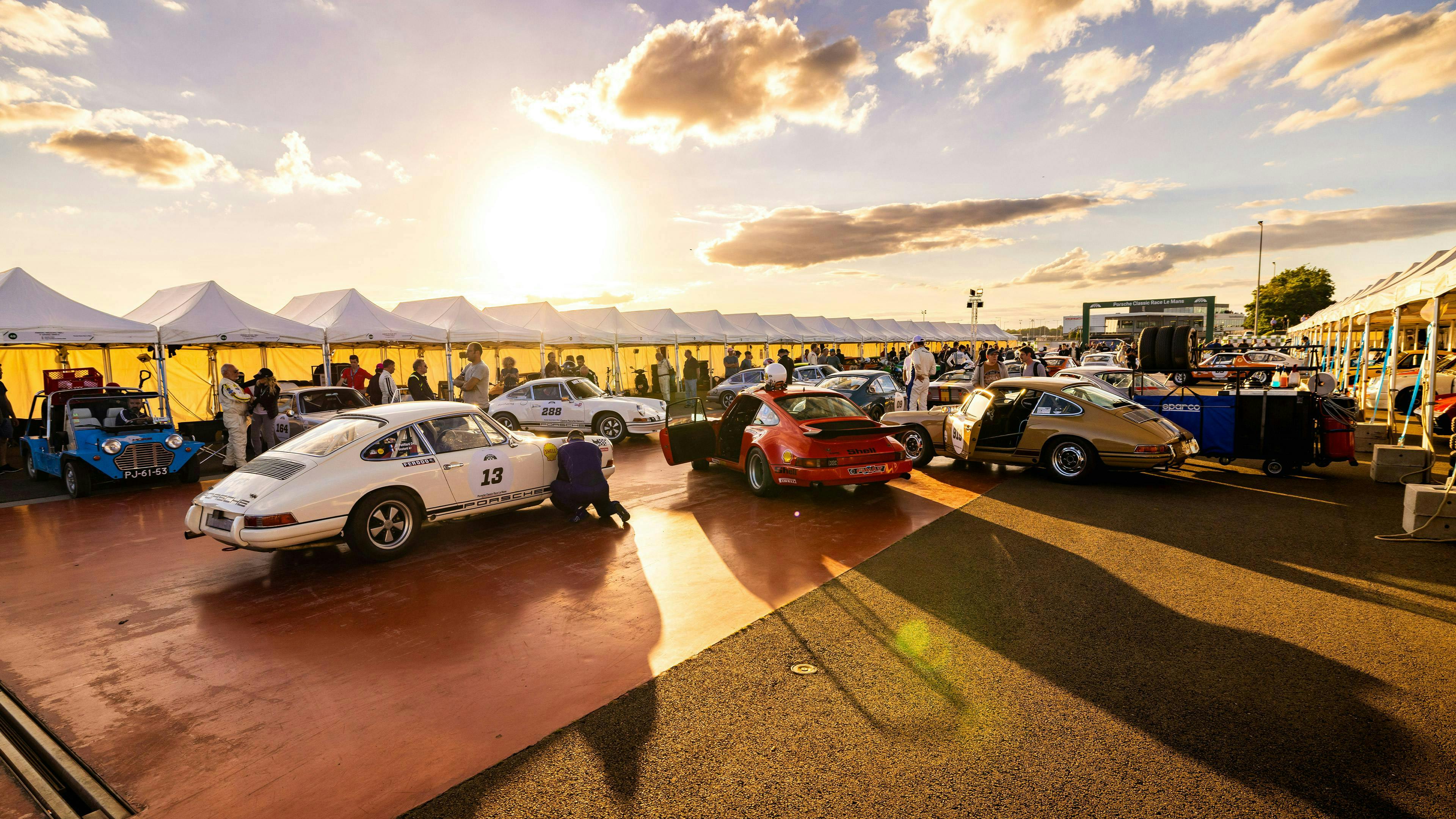 Porsche Club Mitglieder mit verschiedene Porsche Classic Modelle stehen an einer Promenade.