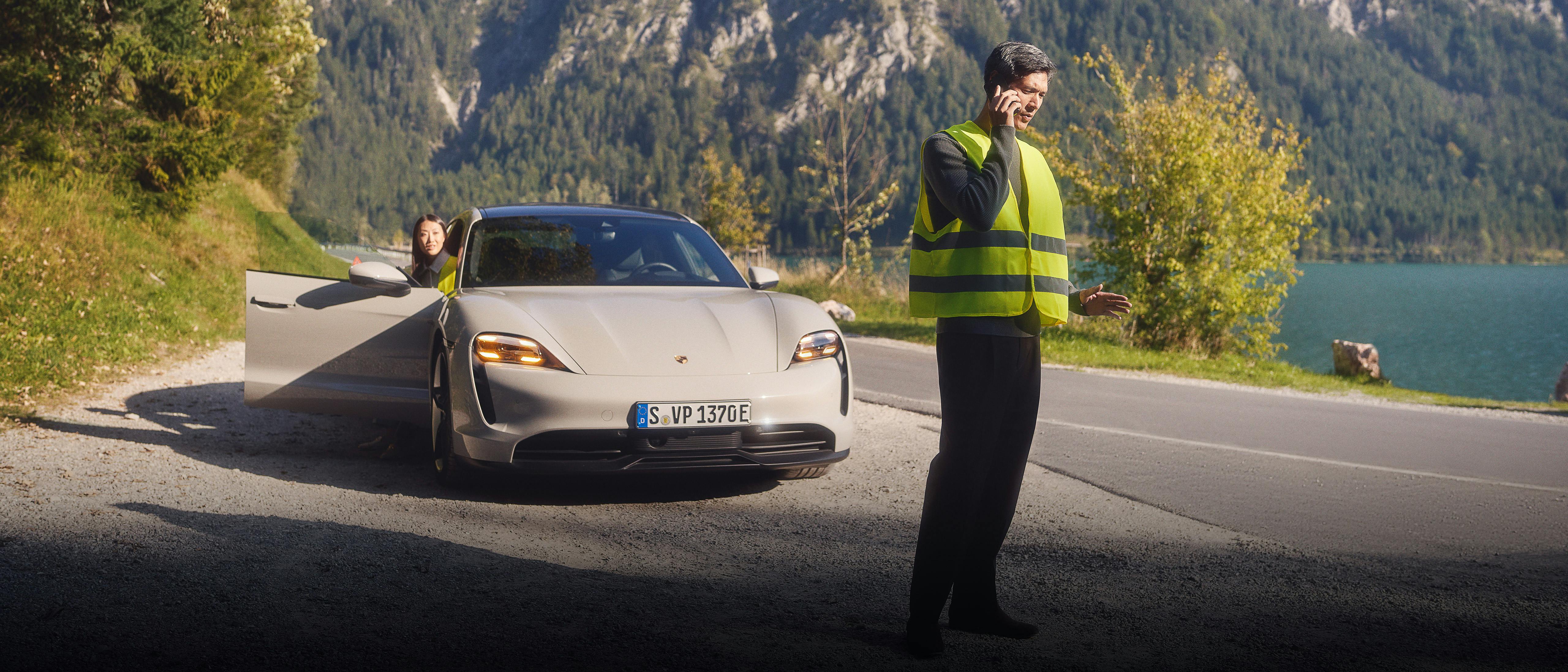 A Porsche Taycan is parked on the side of the road. A woman is getting out of the car while her husband is talking on his mobile phone in front of the car.