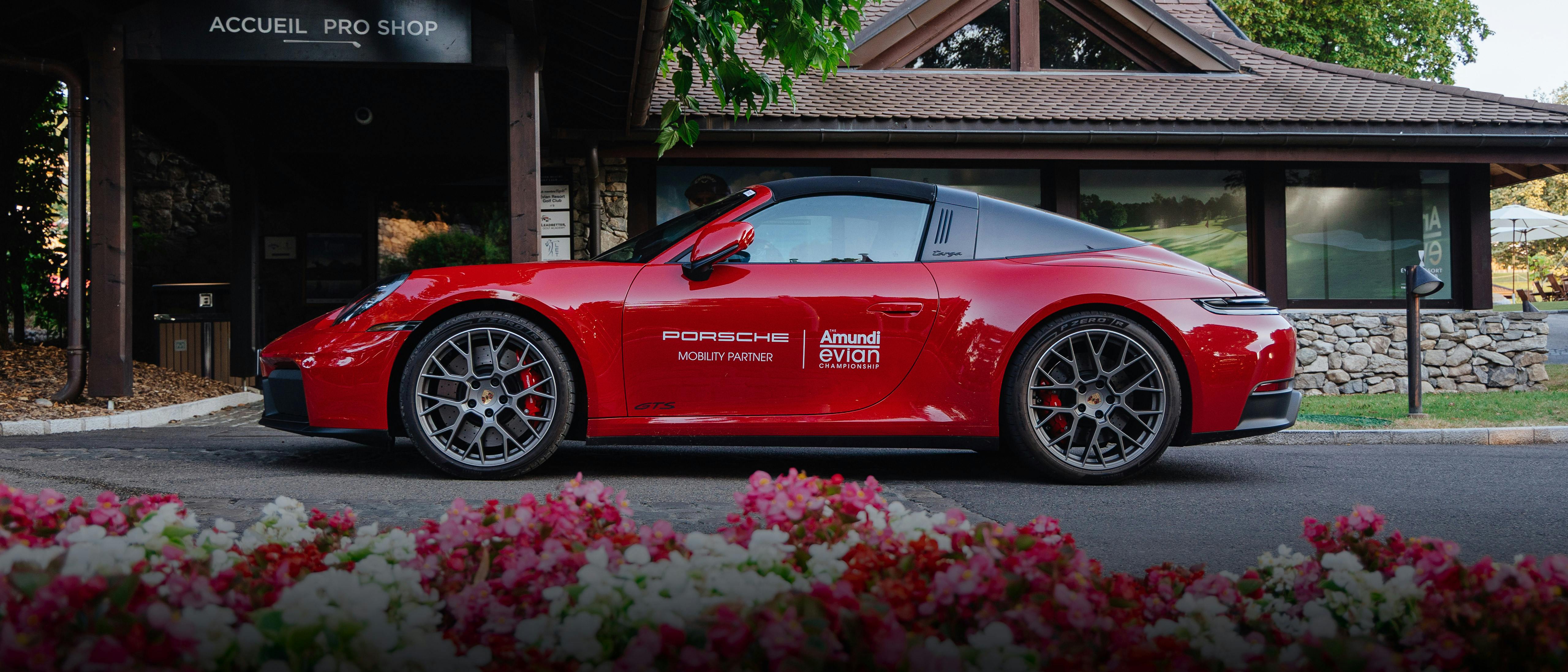 Roter Porsche 911 Targa GTS vor dem Golf-Clubhaus in Evian mit Blumenbeet im Vordergrund.